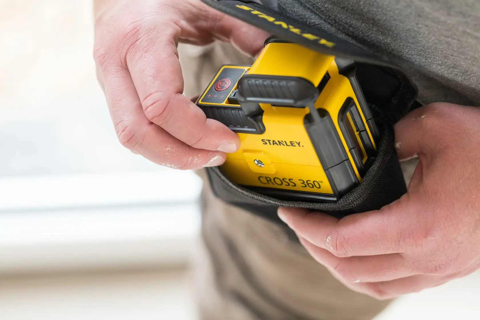 Photo of STANLEY STHT77640-1 CROSS 360° laser level being placed into a black carrying pouch by hand.