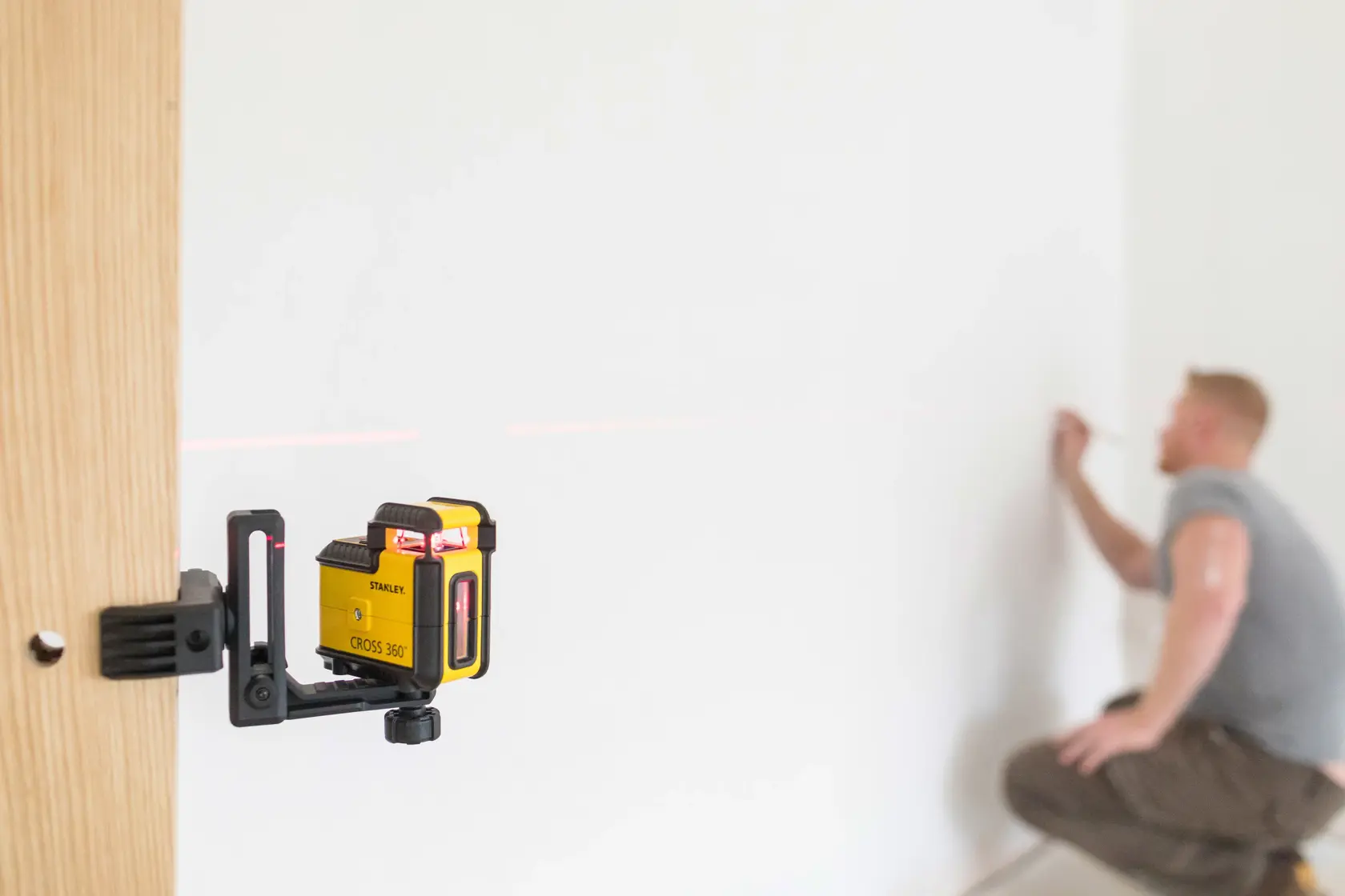 STANLEY STHT77640-1 laser level mounted on wood, projecting red line onto wall for alignment.