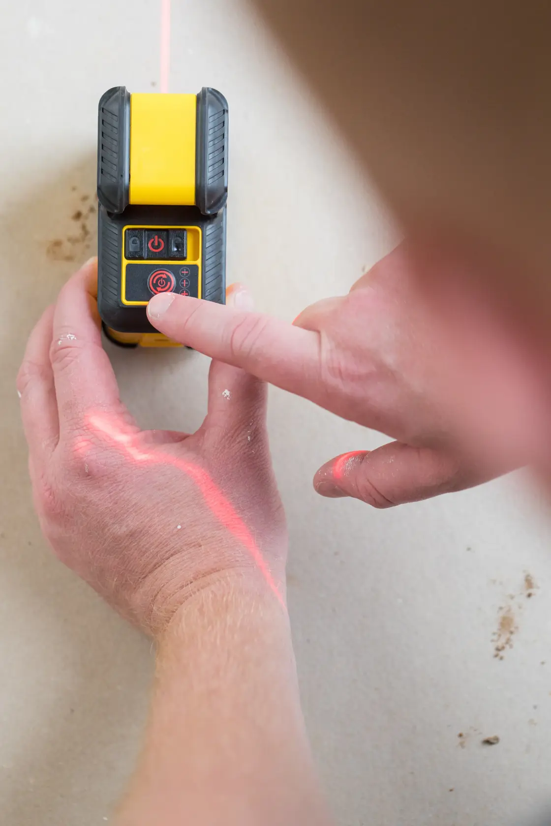 STANLEY STHT77640-1 laser level in use, hand pressing button with red laser line on surface.