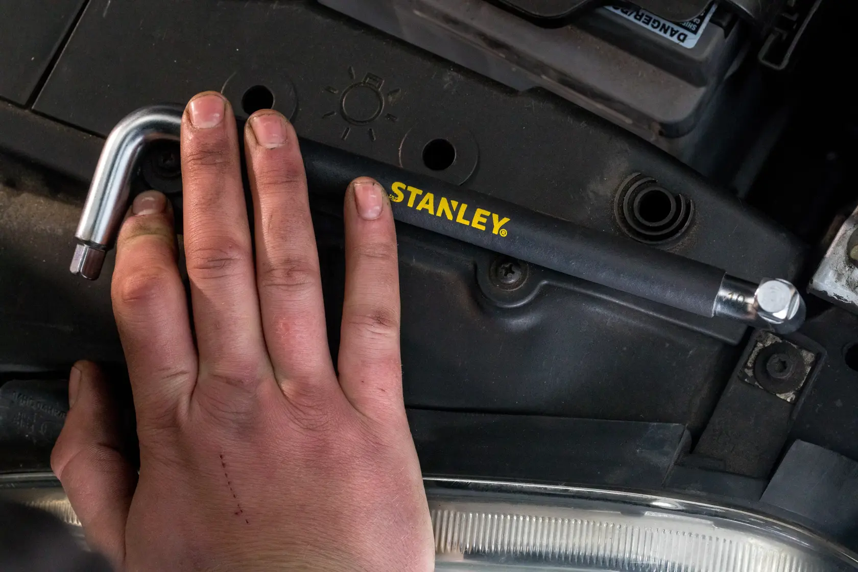 Photo of STANLEY STHT80879-0 L-shaped tool held by hand, shown in automotive engine context.