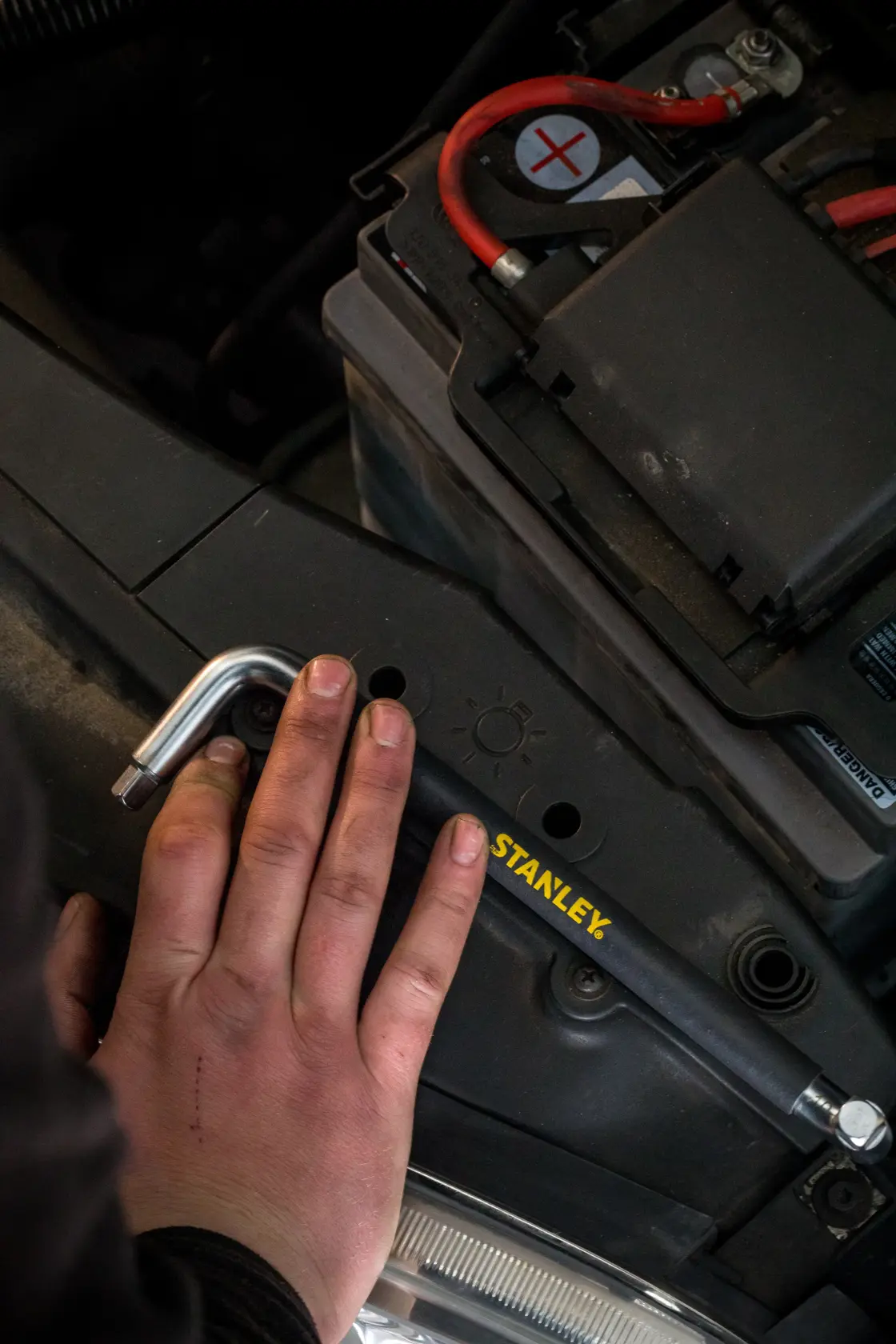 Photo of STANLEY STHT80879-0 hex key in use on a car battery, close-up view with hand holding tool.