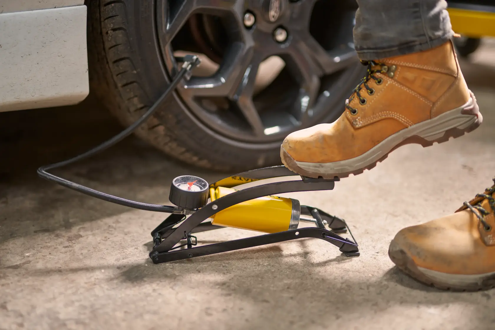 STANLEY STHT80894-1 foot pump inflating car tire, yellow and black, photography of product in use.