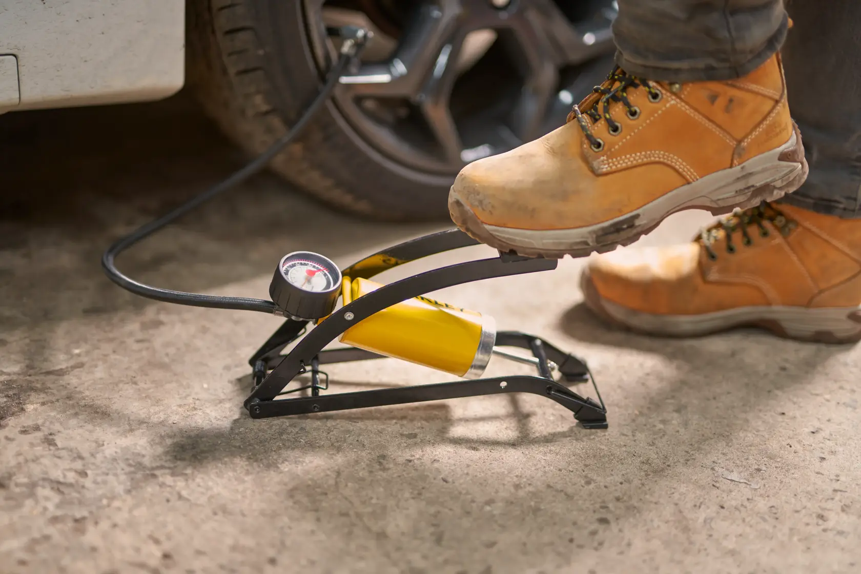 STANLEY STHT80894-1 foot-operated air pump with gauge inflating car tire, close-up in workshop.