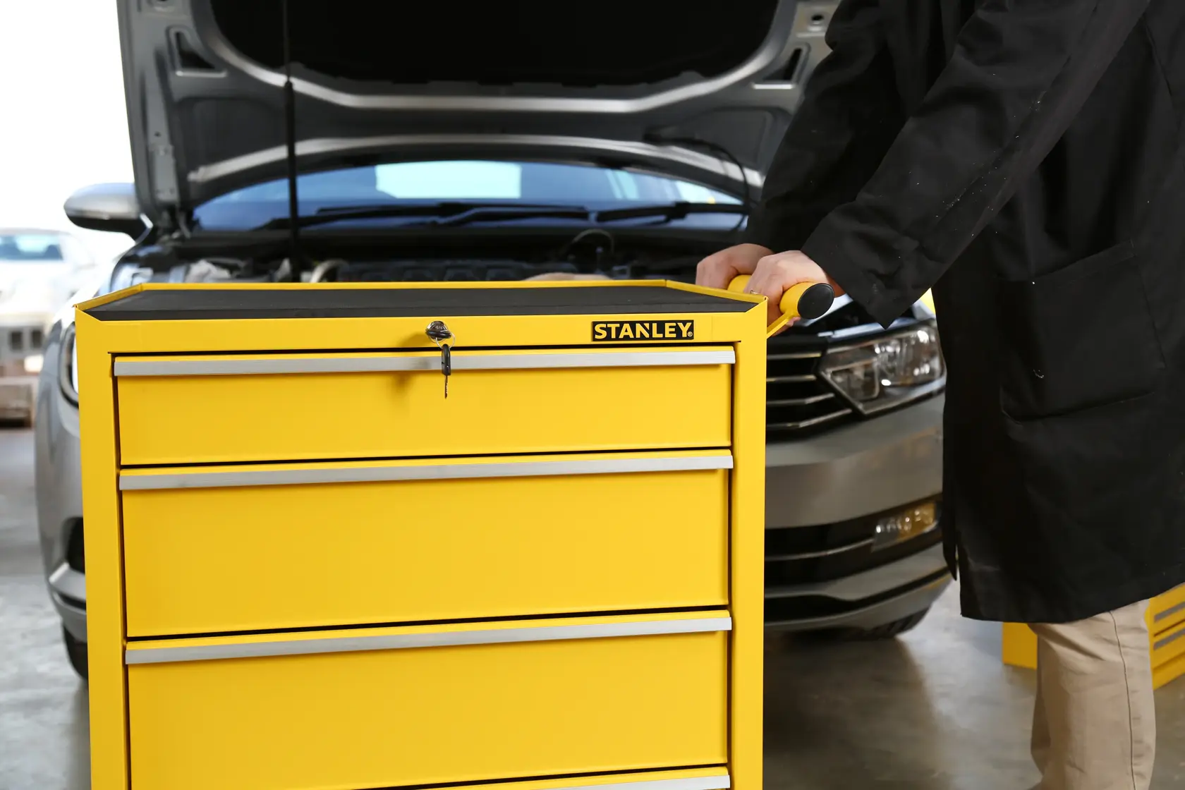 Stanley STMT1-75063 yellow tool chest with four drawers, photographed in a garage setting next to a car.