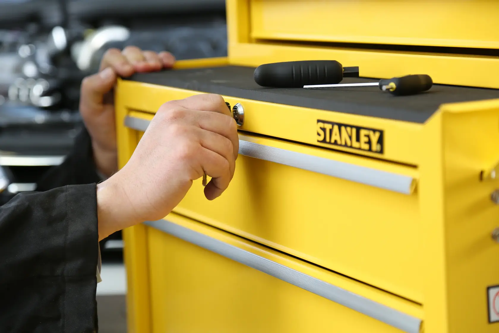Photo of STANLEY STMT1-75063 yellow tool chest drawer being locked by hand, tools on top.
