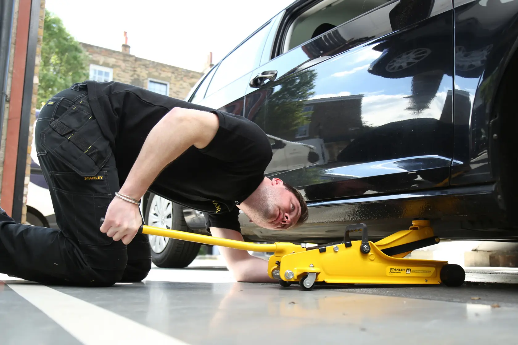 Photo of STANLEY STMT81251-1 hydraulic floor jack in use, lifting a black car by its side.