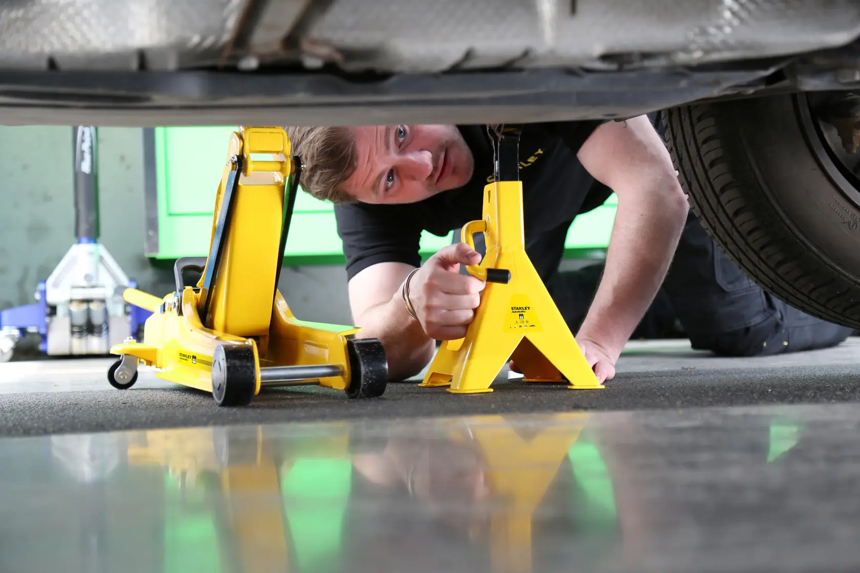Photo of STANLEY STMT81255-1 yellow car jack and stand under vehicle, automotive tool usage scene.