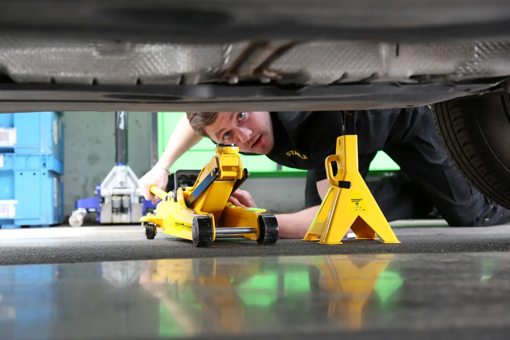 STANLEY STMT81255-1 yellow car jack and jack stand under a vehicle, side angle photo.