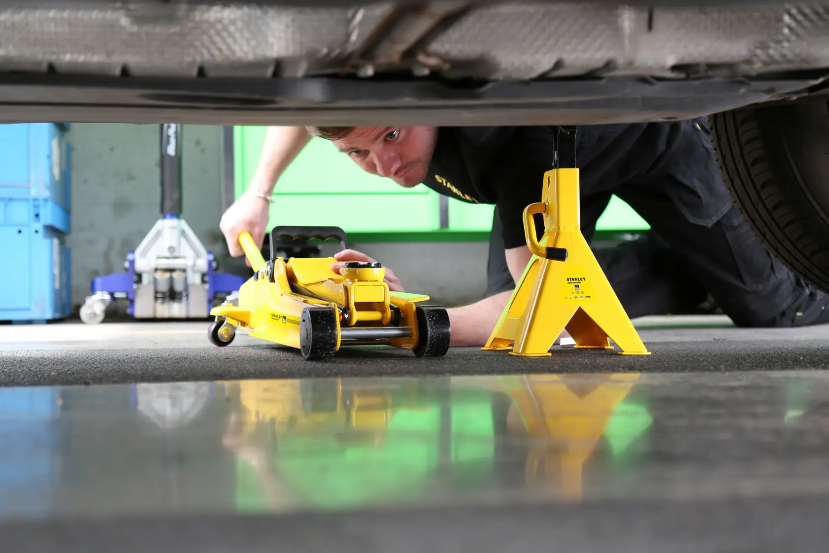STANLEY STMT81255-1 yellow jack stand and floor jack under car, side angle, automotive tool application.