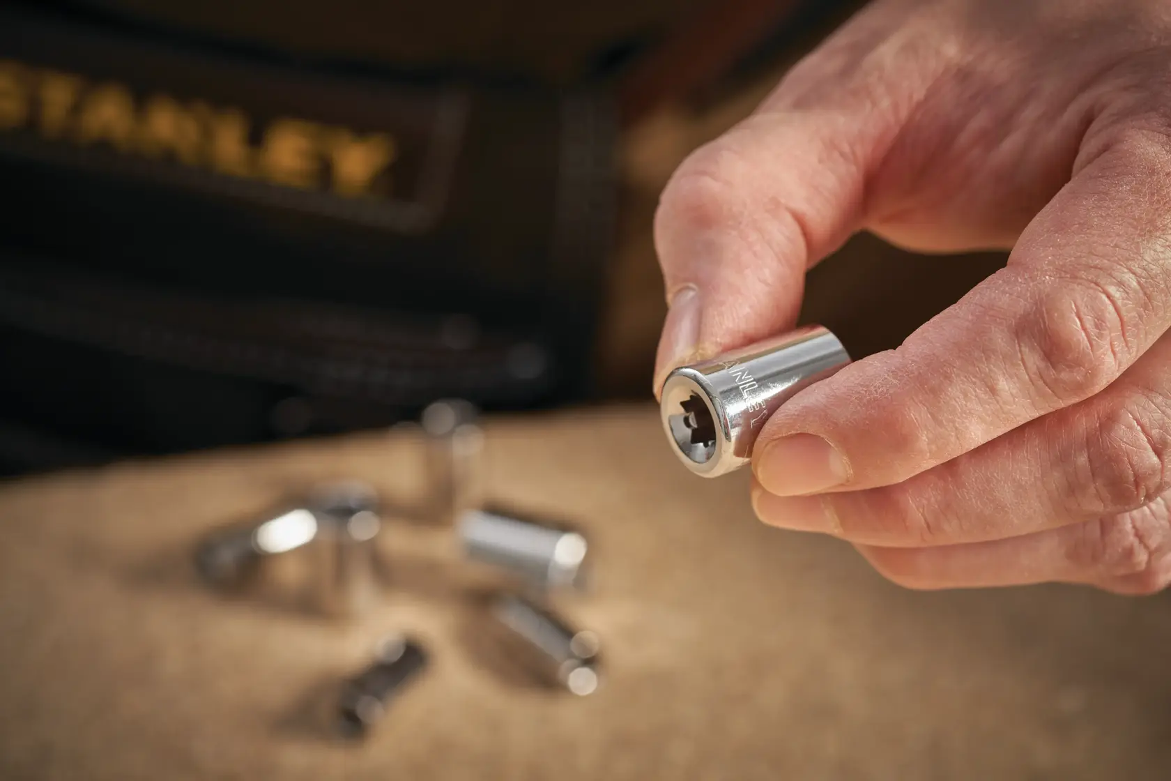 STANLEY STMT86108-0 socket held in hand, chrome finish, with other sockets blurred in background.