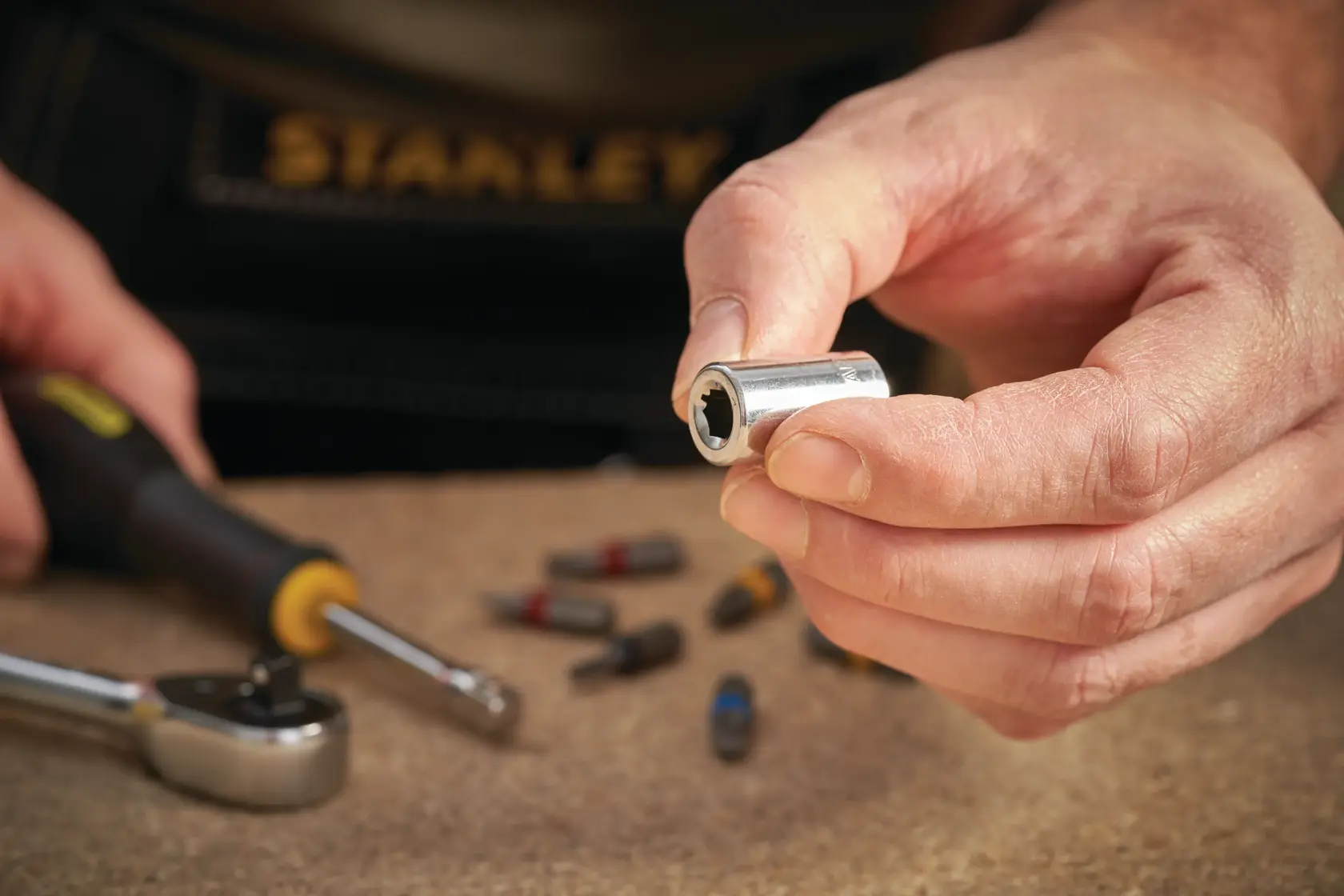 Photo of STANLEY STMT86124-0 socket held in hand, with ratchet and bits on workbench.