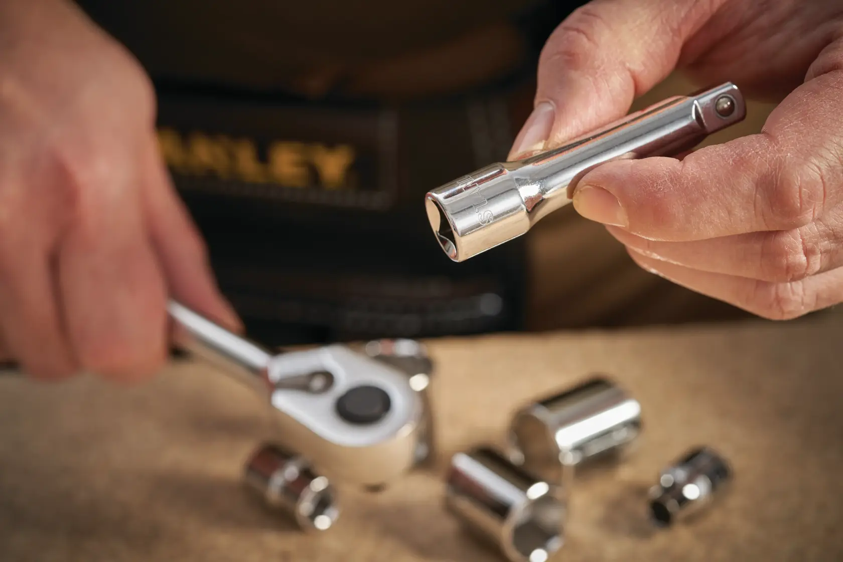 STANLEY STMT86206-0 socket wrench extension held by hand, with ratchet and sockets on workbench.