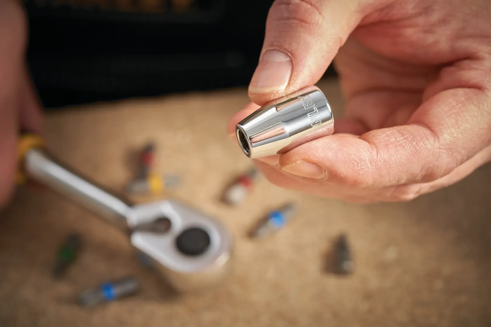 Photo of STANLEY STMT86250-0 socket bit held by hand, ratchet and bits on work surface.