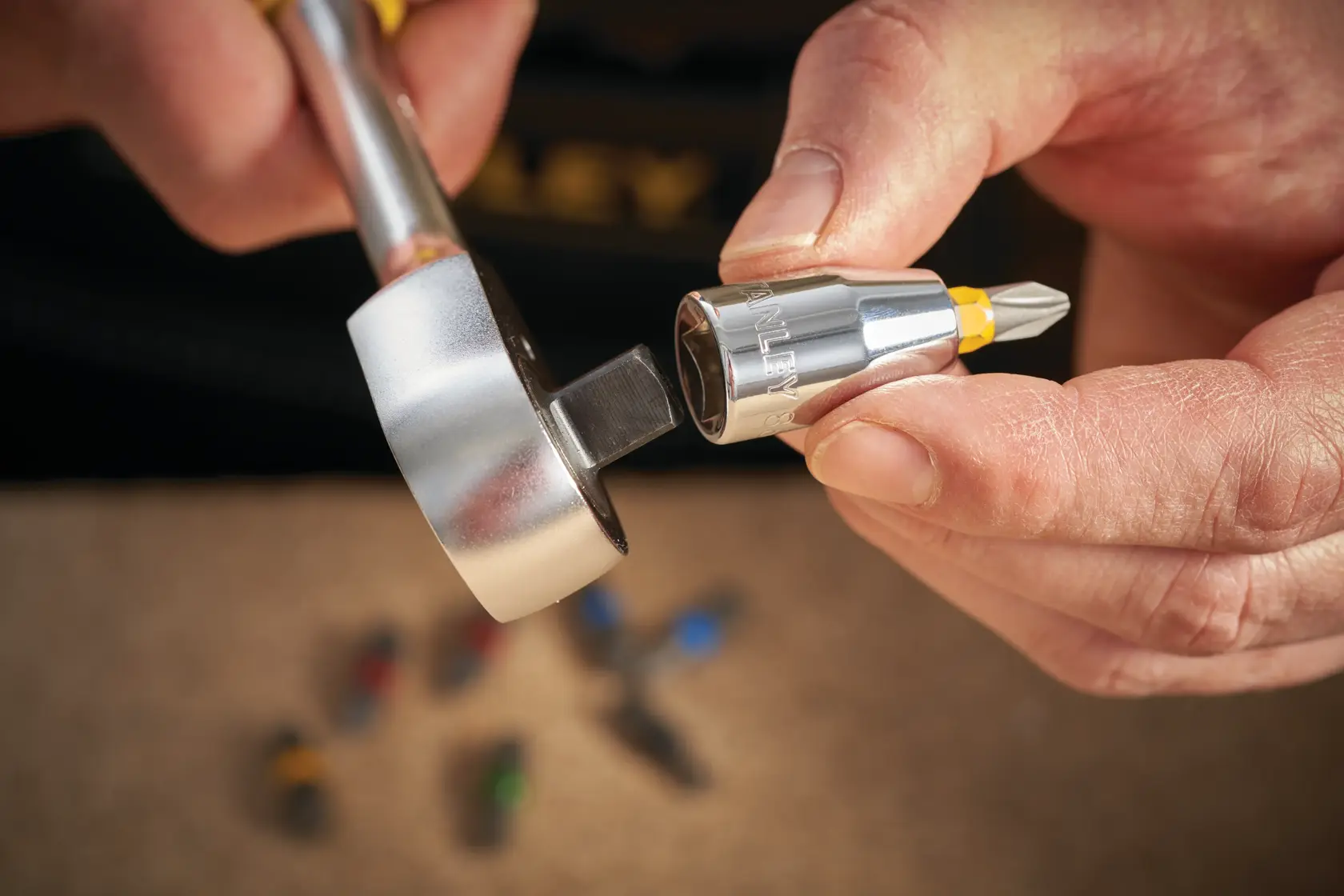 STANLEY STMT86250-0 ratchet with a screwdriver bit adapter in hand, close-up, tool set in background.
