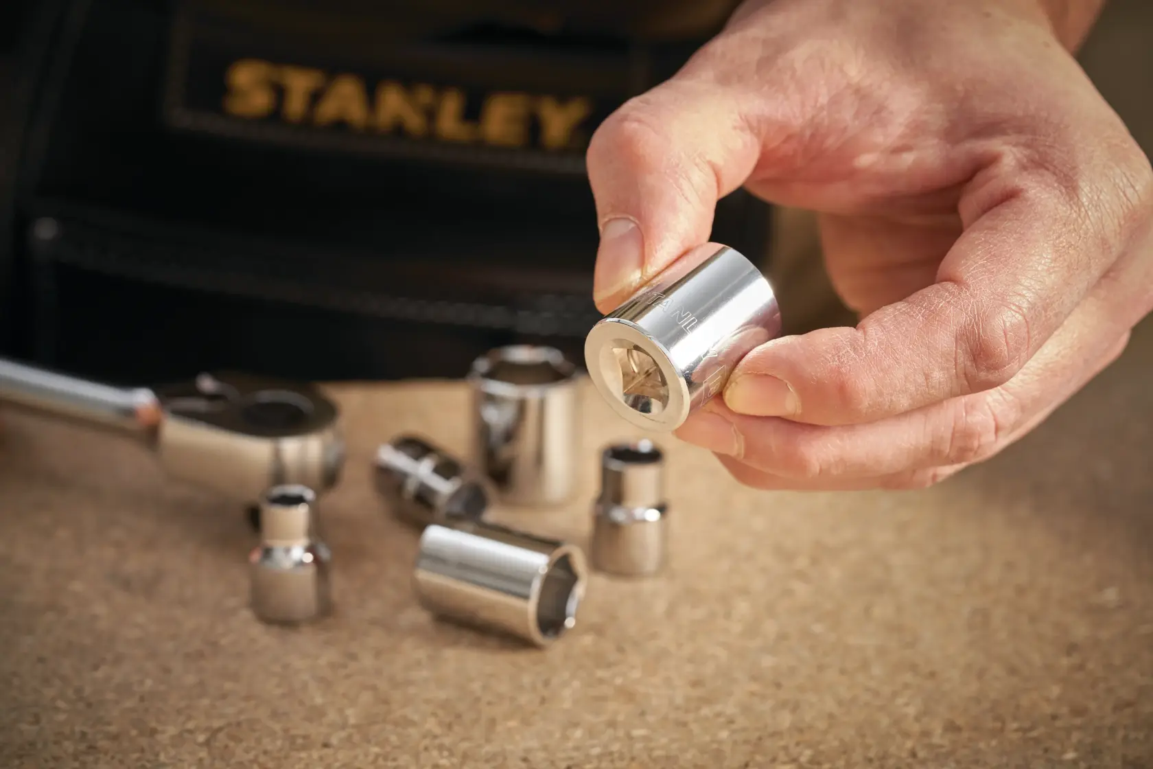 STANLEY STMT86315-0 chrome socket set with hand holding socket, close-up with ratchet and sockets on work surface.