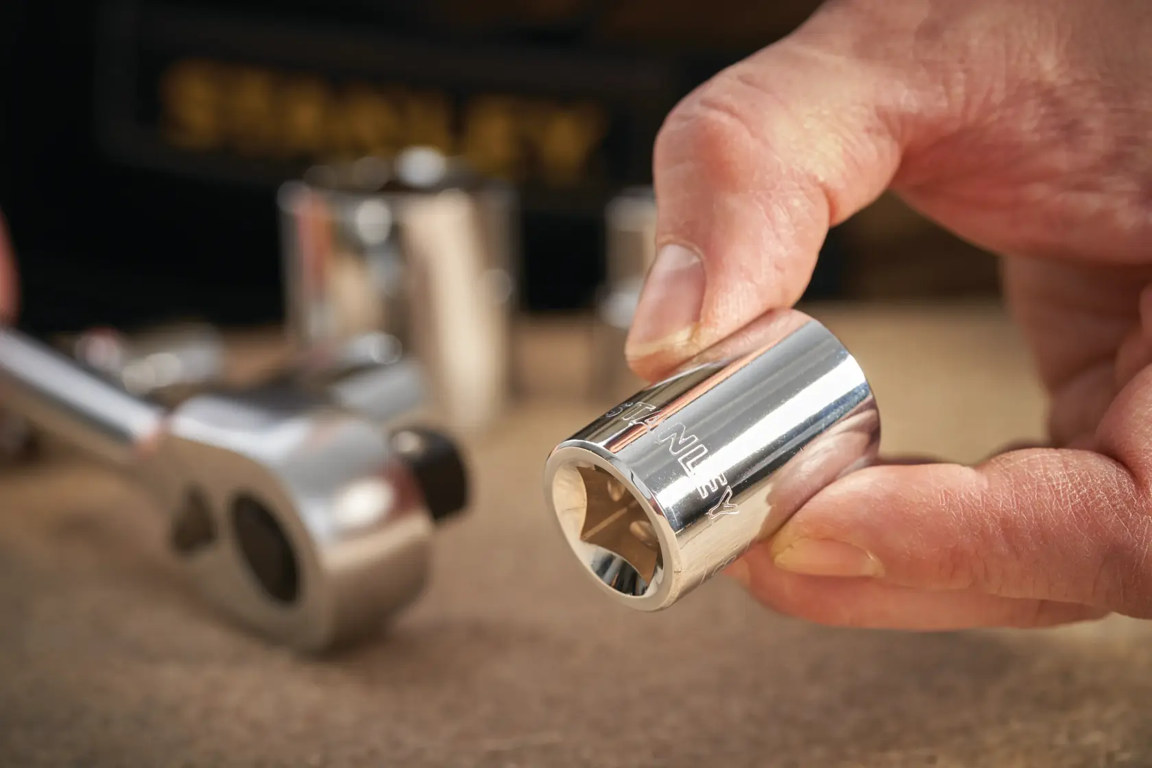 Photo of STANLEY STMT86517-0 chrome socket held by hand, with ratchet and other sockets in background.
