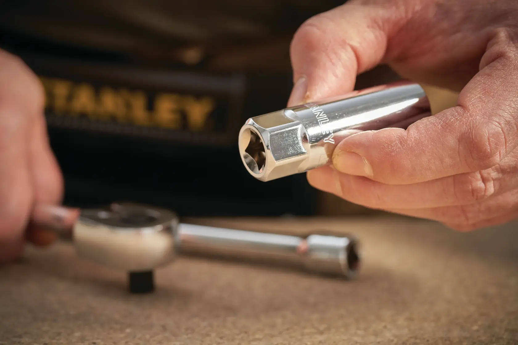 Photo of STANLEY STMT88942-0 chrome socket tool held in hand, with ratchet wrench on table.
