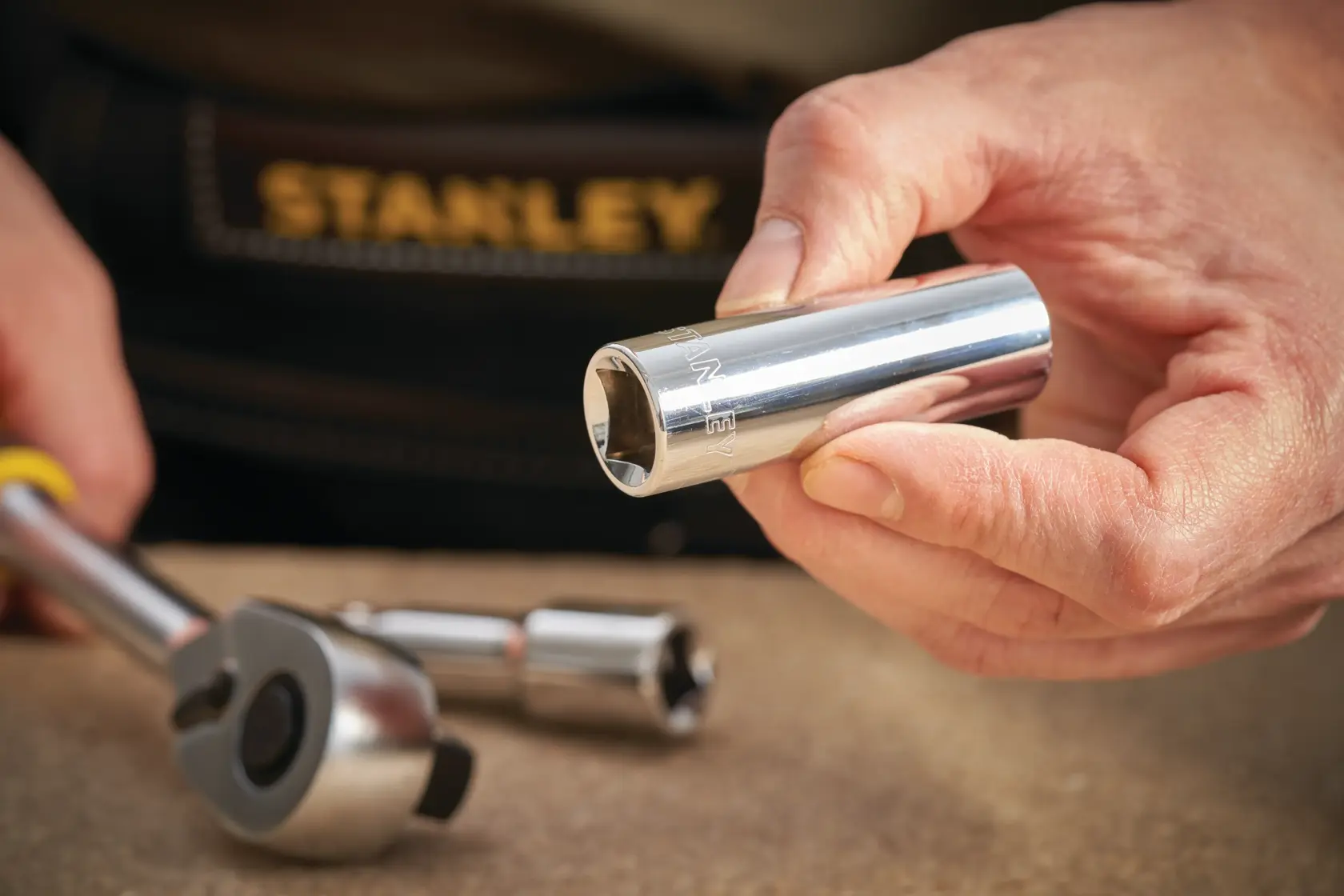 Photo of STANLEY STMT88994-0 chrome socket tool held by hand, with ratchet and extension on table.