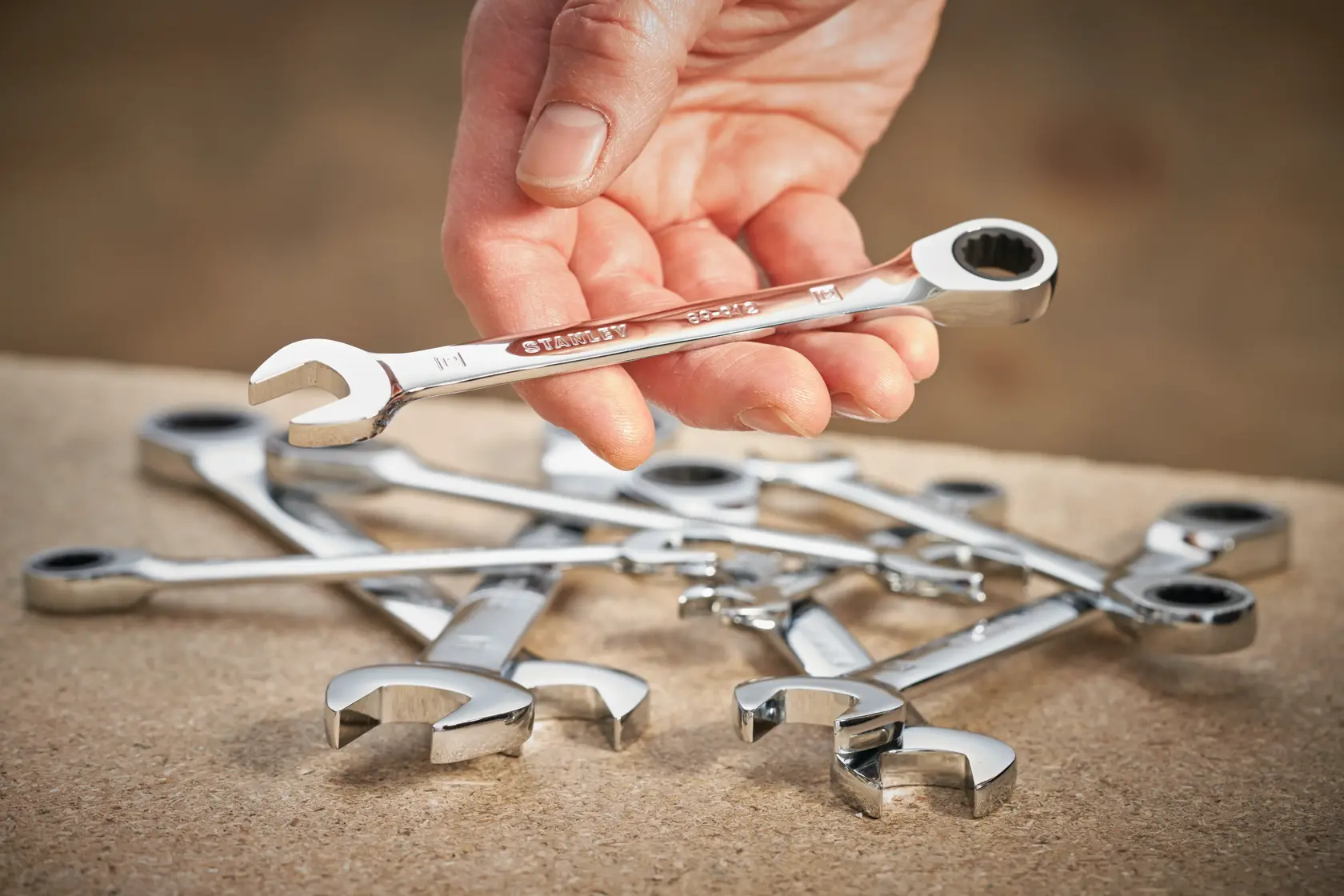 STANLEY STMT89908-0 combination wrenches photo, hand holding chrome wrench, tools on workbench.