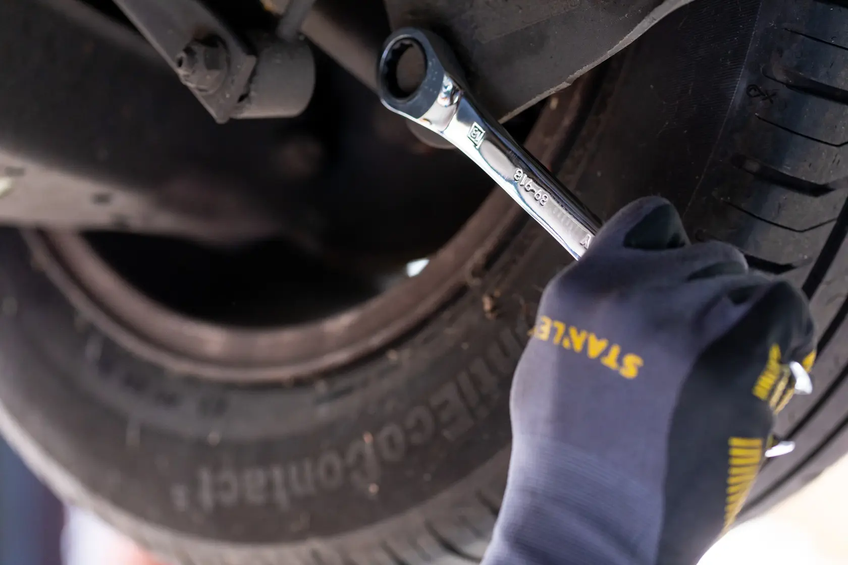 STANLEY STMT89908-0 ratcheting wrench used on car wheel bolt, close-up with gloved hand.