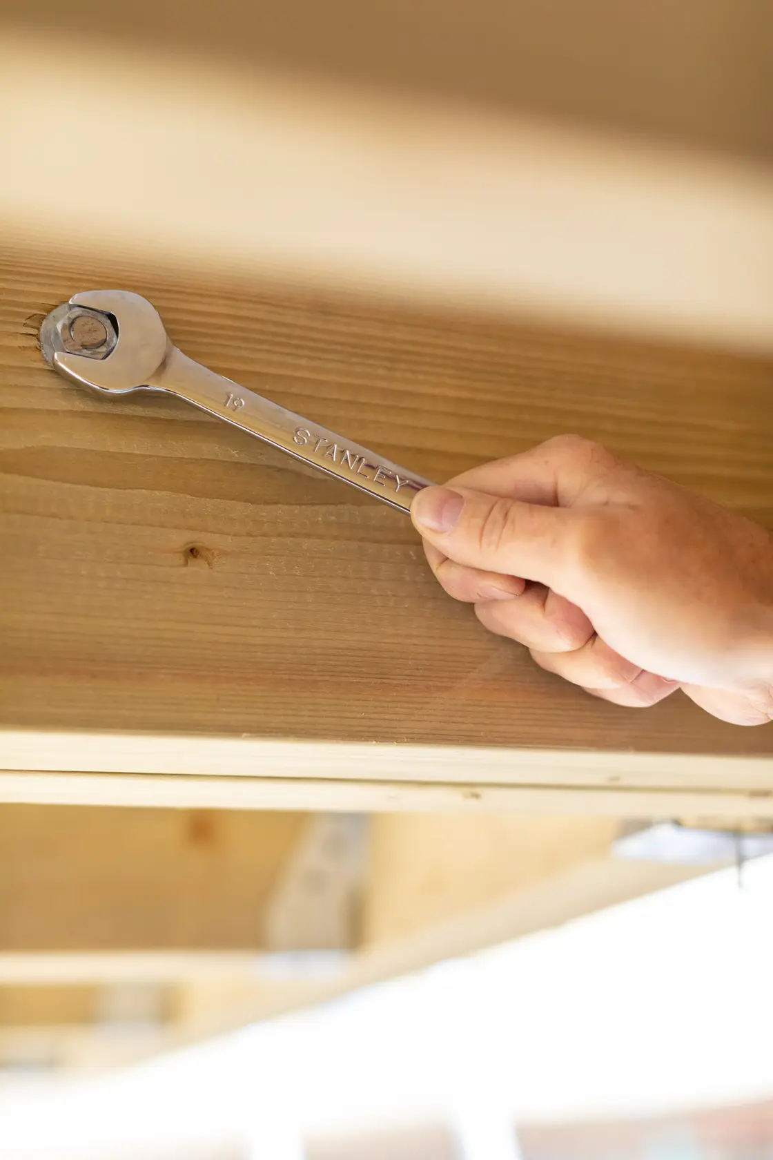 Photo of STANLEY STMT89913-0 wrench being used to tighten a bolt on wooden beams, close-up view.