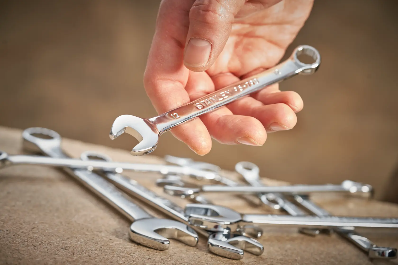 STANLEY STMT95909-0 combination wrench held in hand, with several chrome wrenches on a work surface.