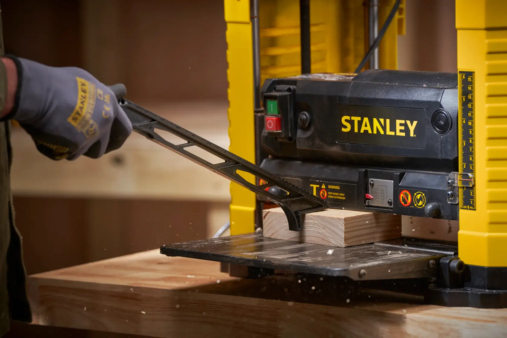 STANLEY STP18-B2 benchtop planer in use, close-up view showing gloved hand adjusting wood piece.