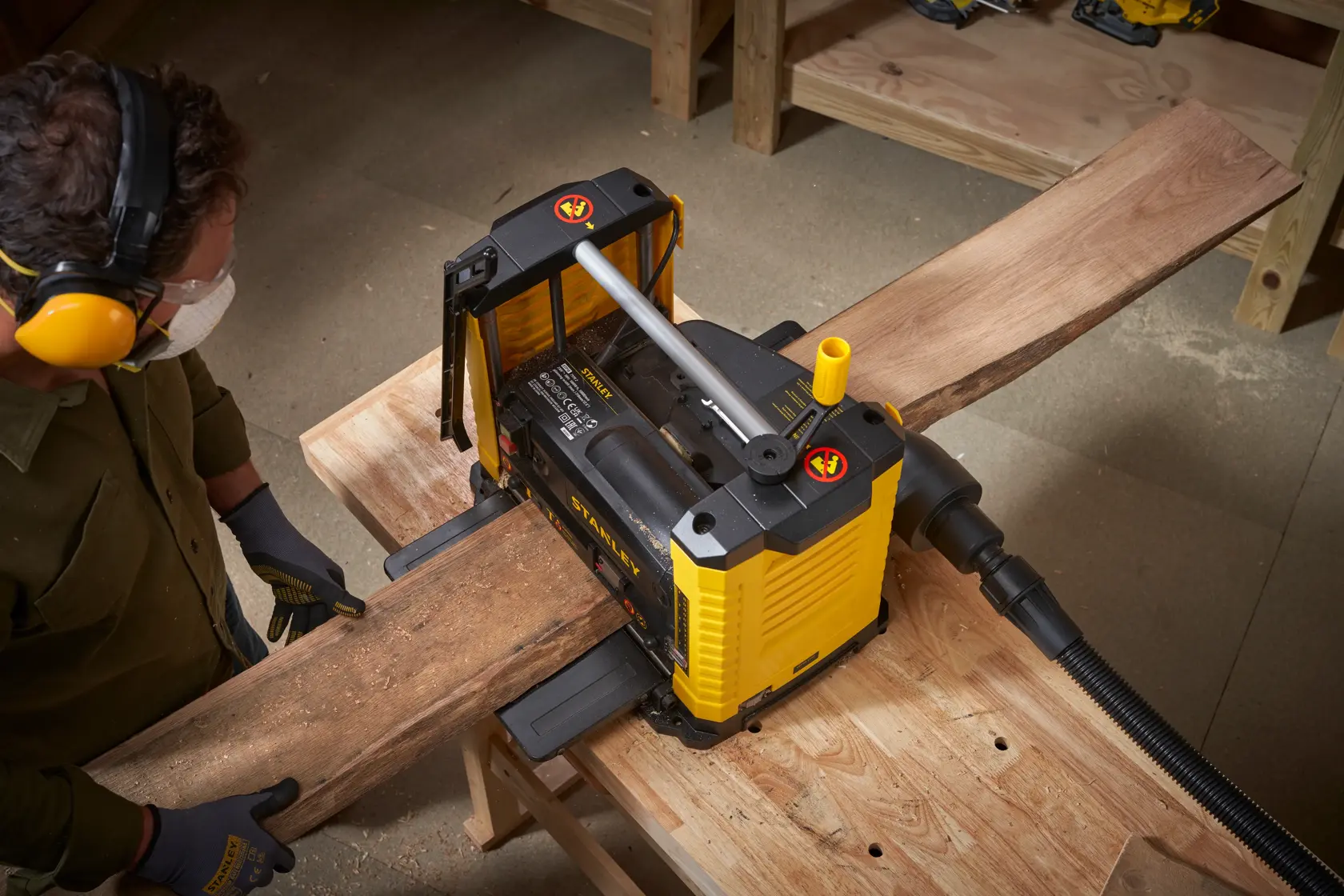 Photo of STANLEY STP18-B2 planer in use, smoothing a wooden board in a workshop from a top angle.