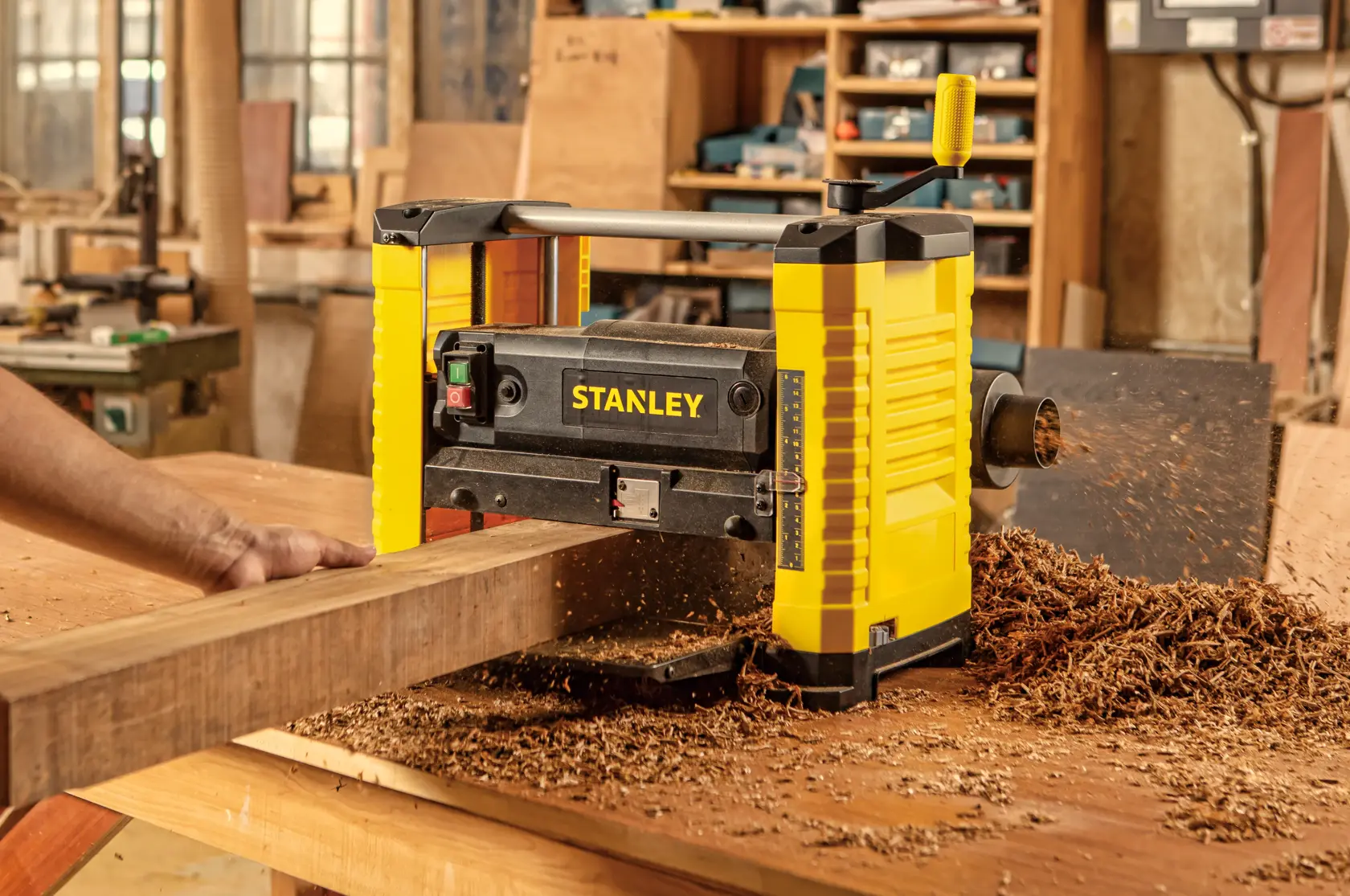 STANLEY STP18-B2 planer in use, yellow and black, wood shavings on workbench in workshop setting.
