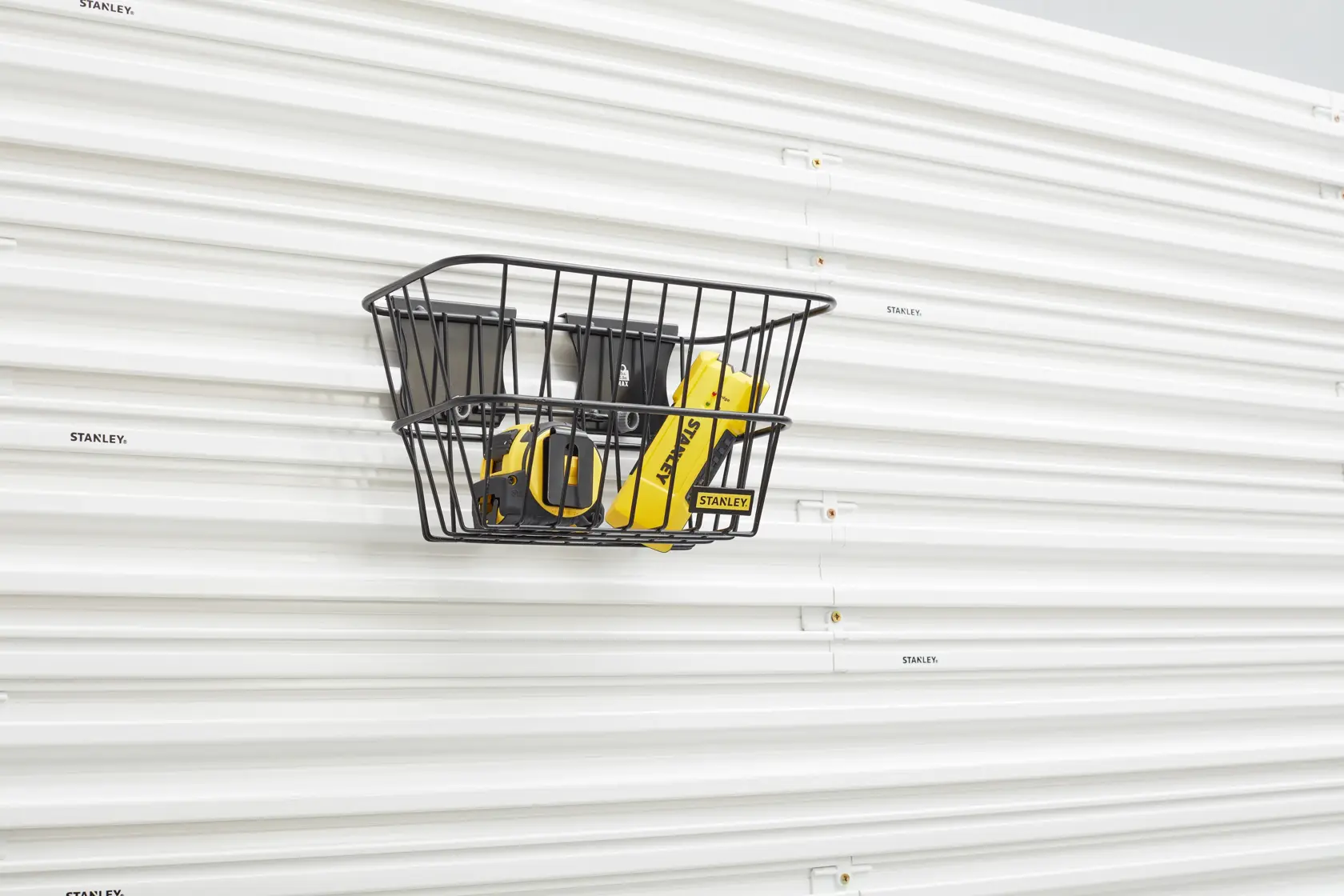 Stanley STST82603-1 black wire storage basket on white slatwall, front angle, holding yellow tools.