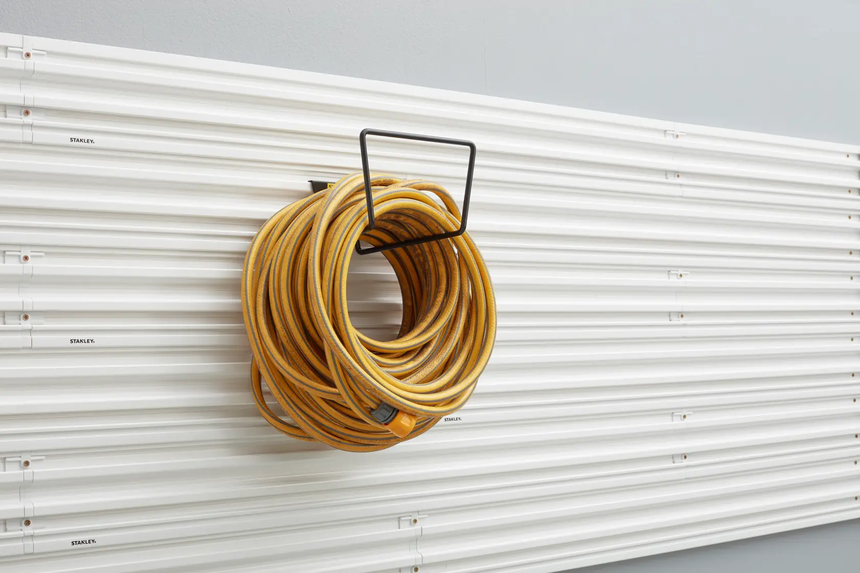 STANLEY STST82604-1 wall-mounted hose holder with yellow hose, front angle, garage organization accessory.