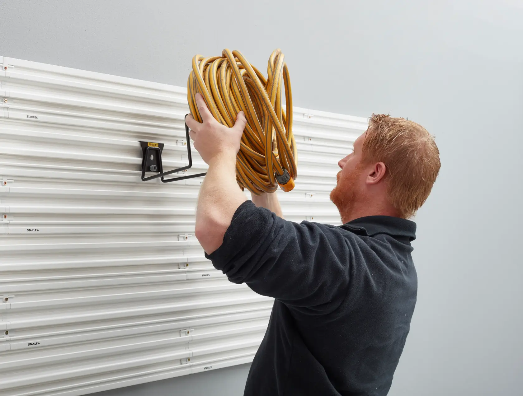 STANLEY STST82604-1 wall-mounted hook holding coiled yellow hose, side angle, for storage organization.