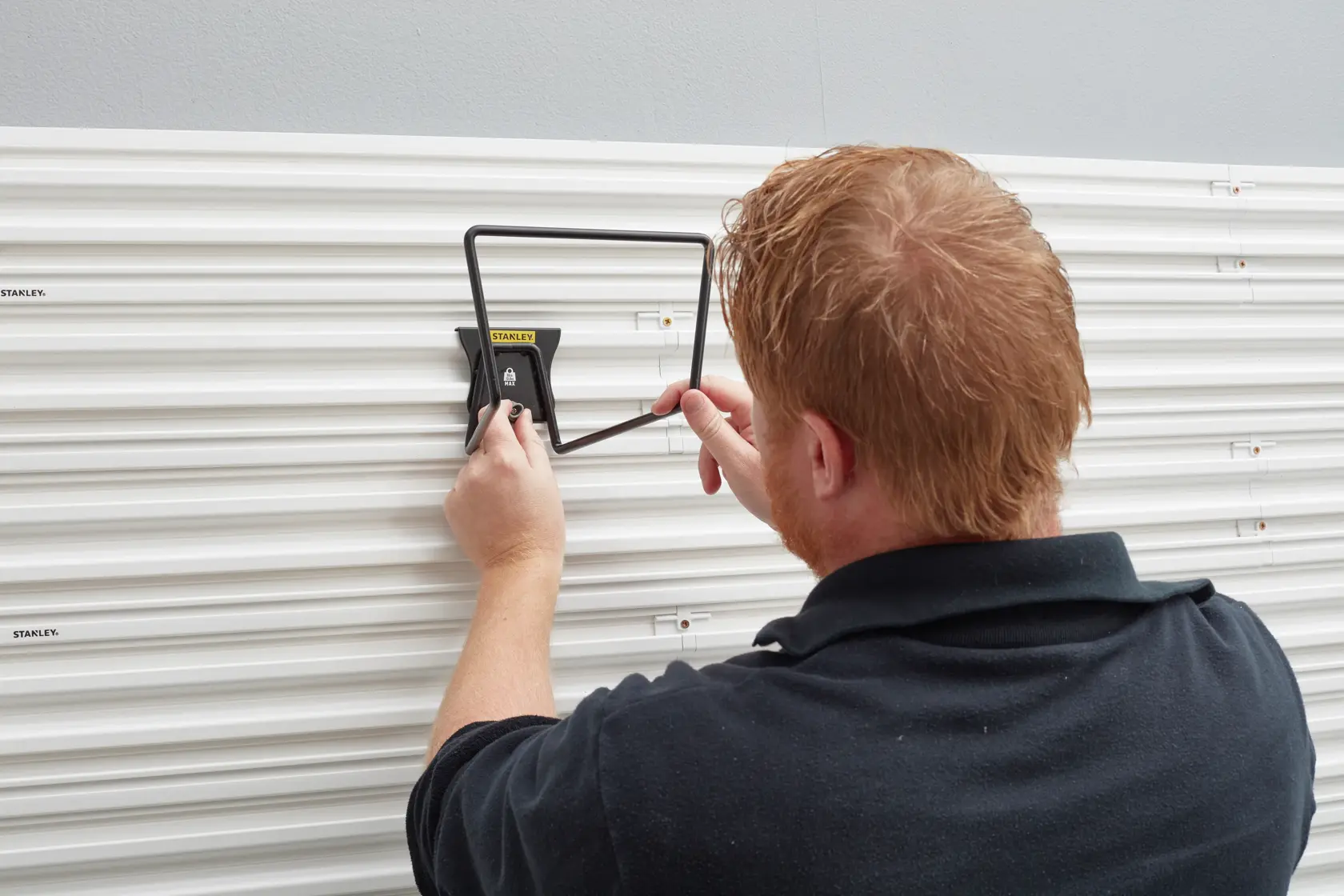 STANLEY STST82604-1 wall storage hook being mounted on white grooved panel, rear angle view.