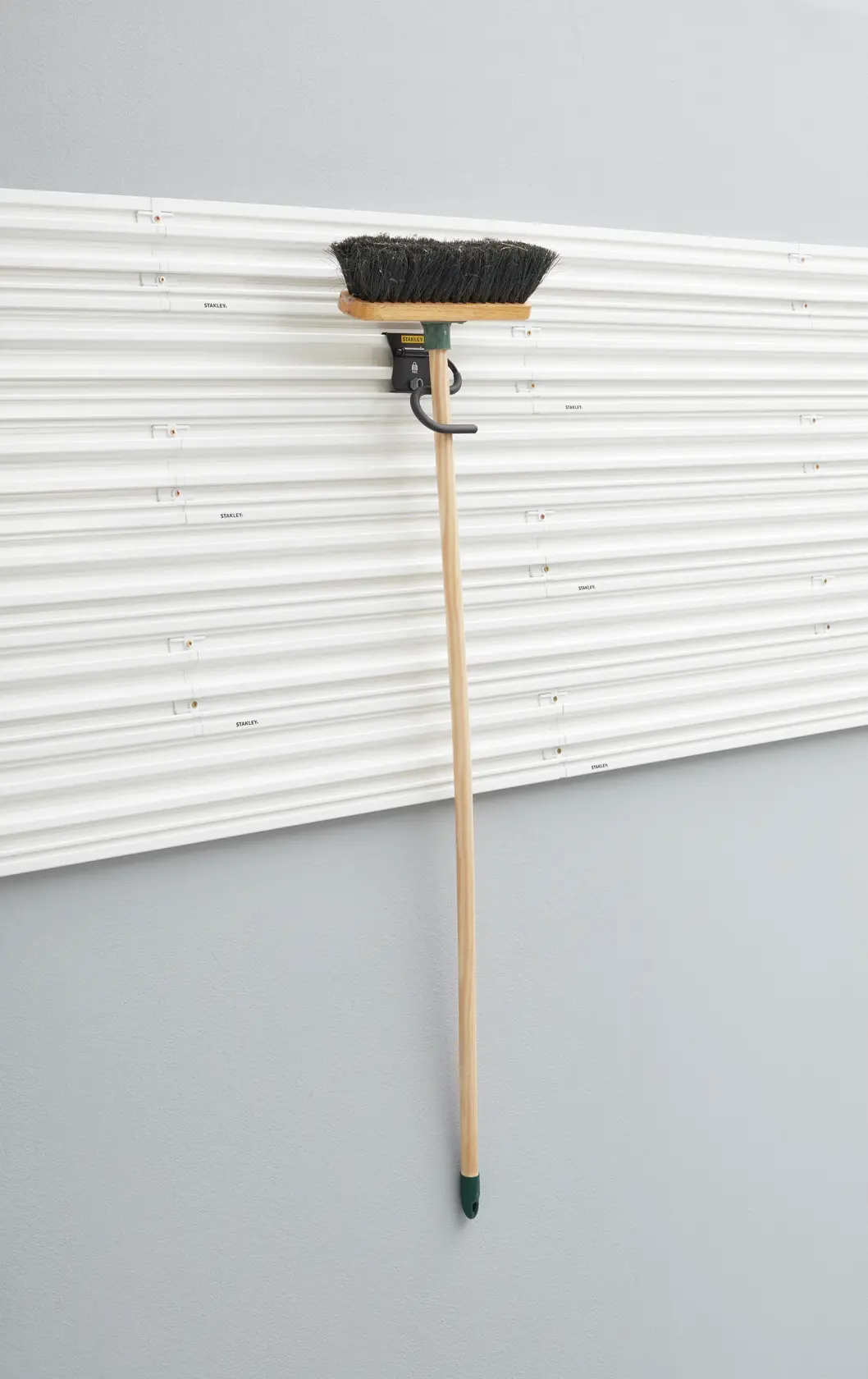 Photo of STANLEY STST82605-1 wall-mounted storage hook holding a broom, shown against a white slat wall.