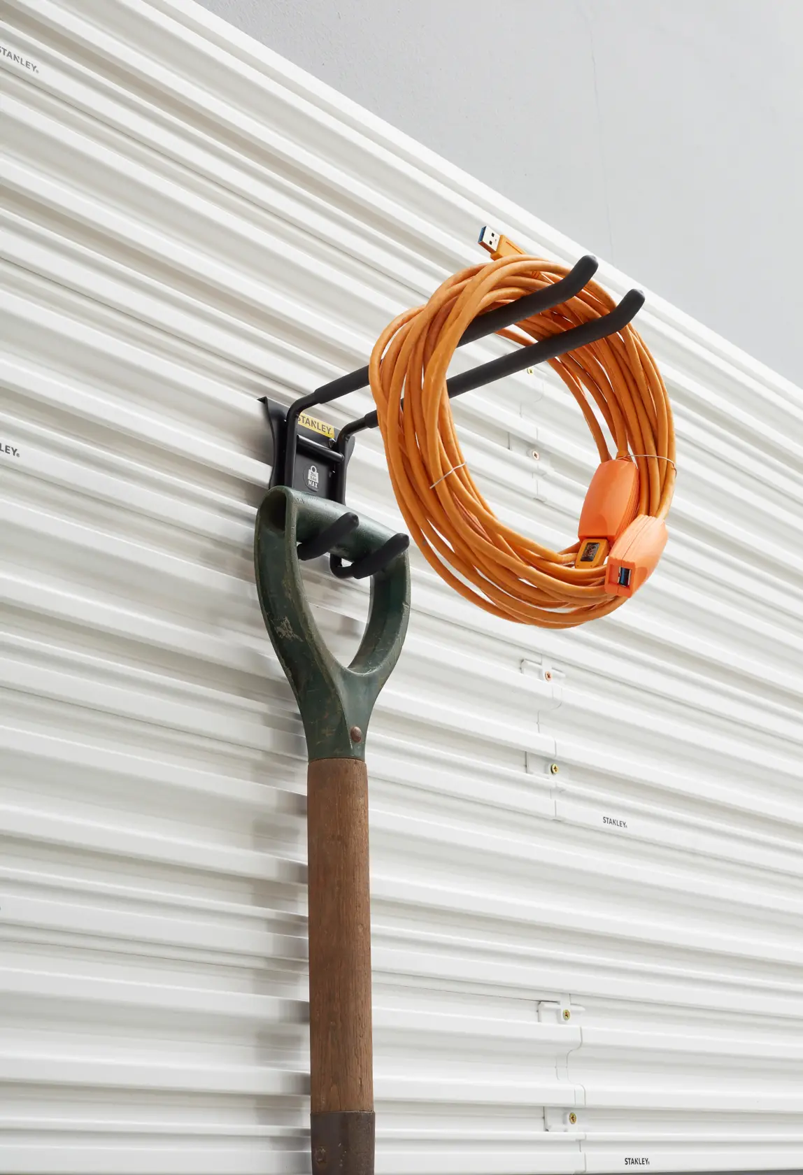STANLEY STST82606-1 wall-mounted hook holding garden tool and orange extension cord, side angle.
