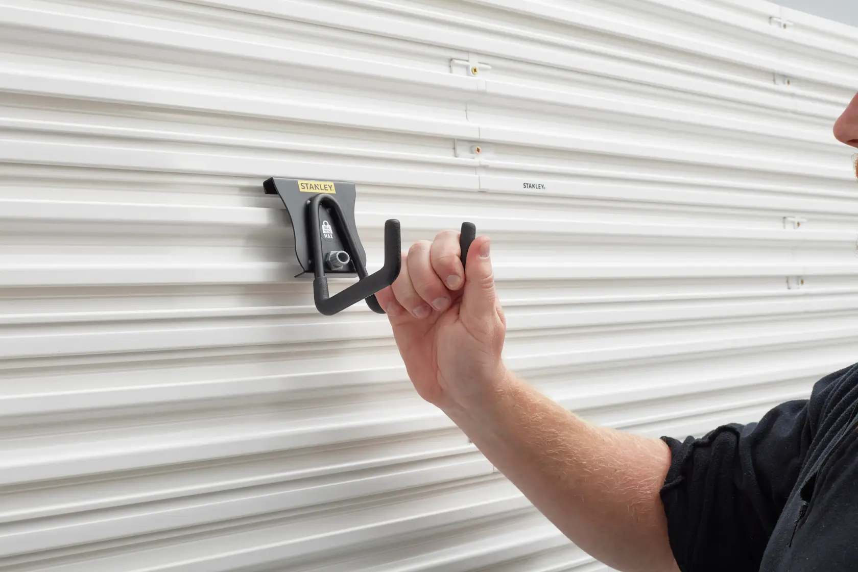 Photo of STANLEY STST82607-1 wall hook being mounted on white grooved panel, close-up view.