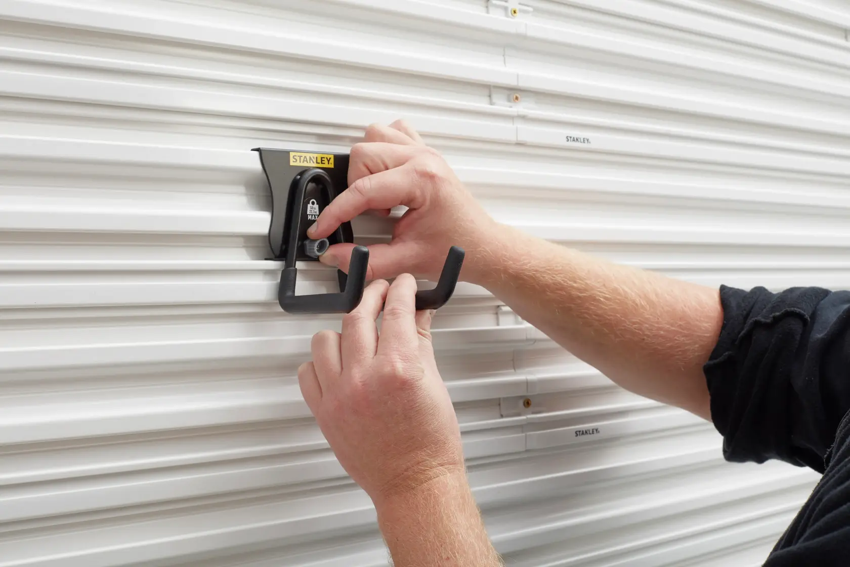 Photo of STANLEY STST82607-1 double hook being mounted on white slatwall, hands adjusting the black hook.