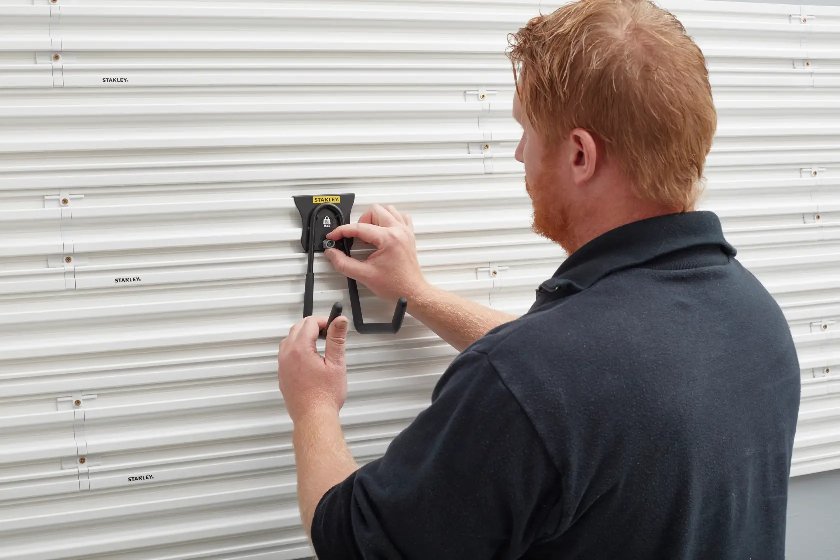Photo of STANLEY STST82608-1 wall hook being installed on white slat wall panel, storage accessory in use.