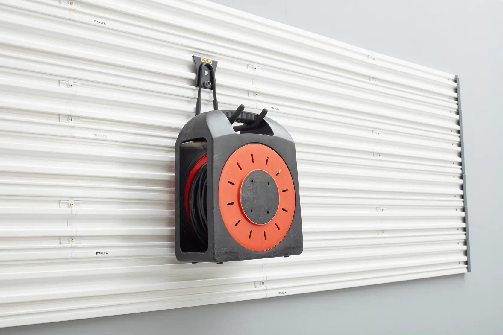 STANLEY STST82608-1 wall-mounted cable reel organizer, black and orange, front angle photo.
