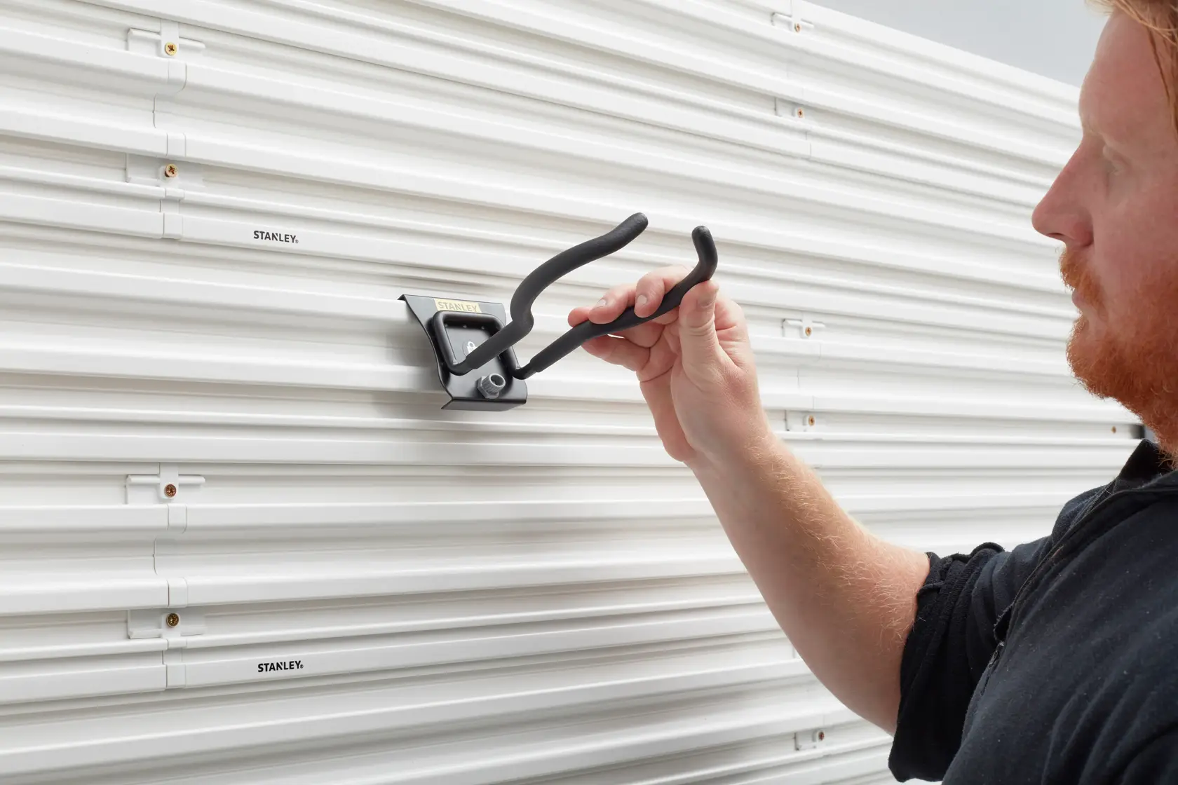 STANLEY STST82609-1 wall-mounted storage hook being installed on white slatwall panel.