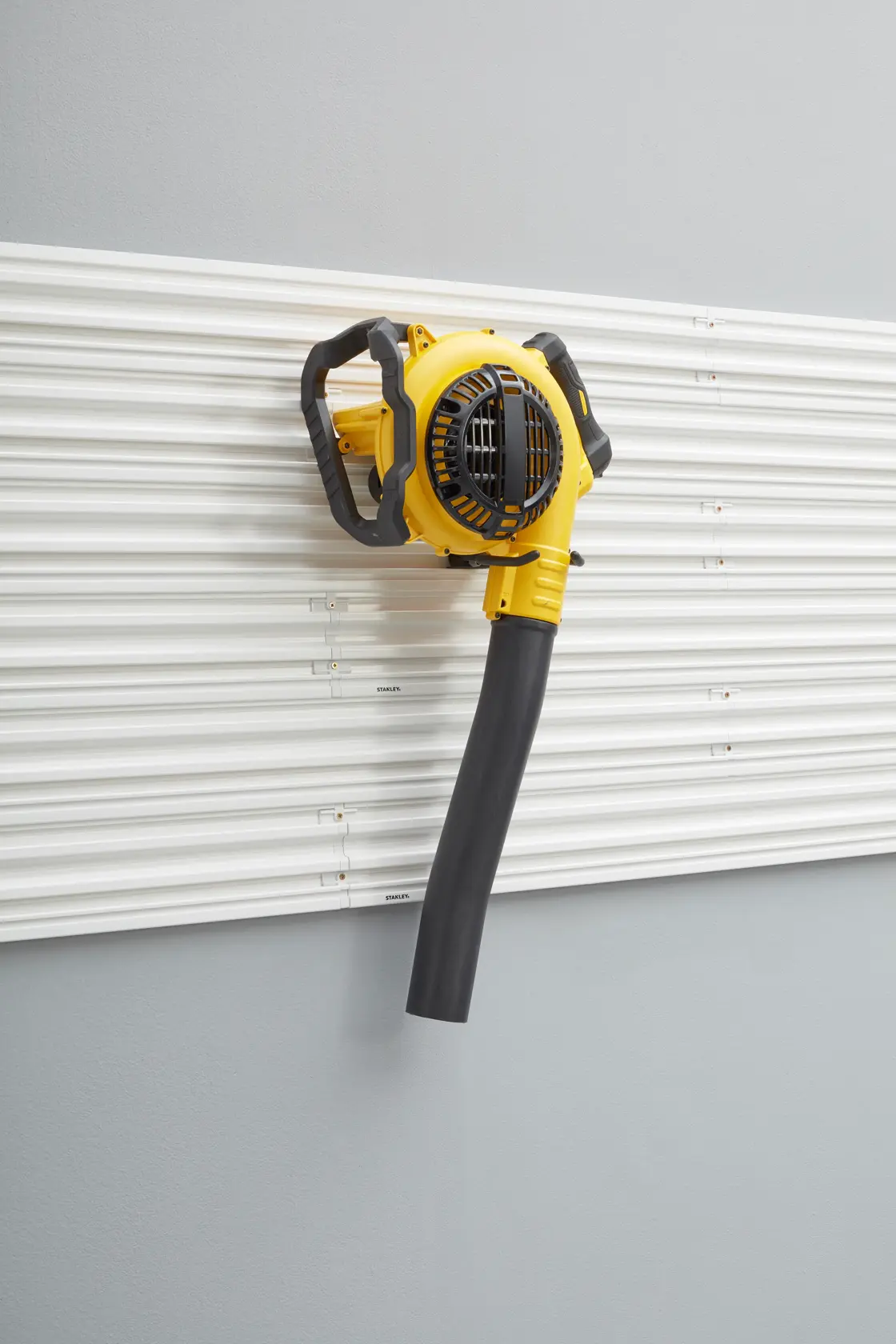 STANLEY STST82609-1 wall-mounted yellow blower with black nozzle, front angle, on white slat wall.