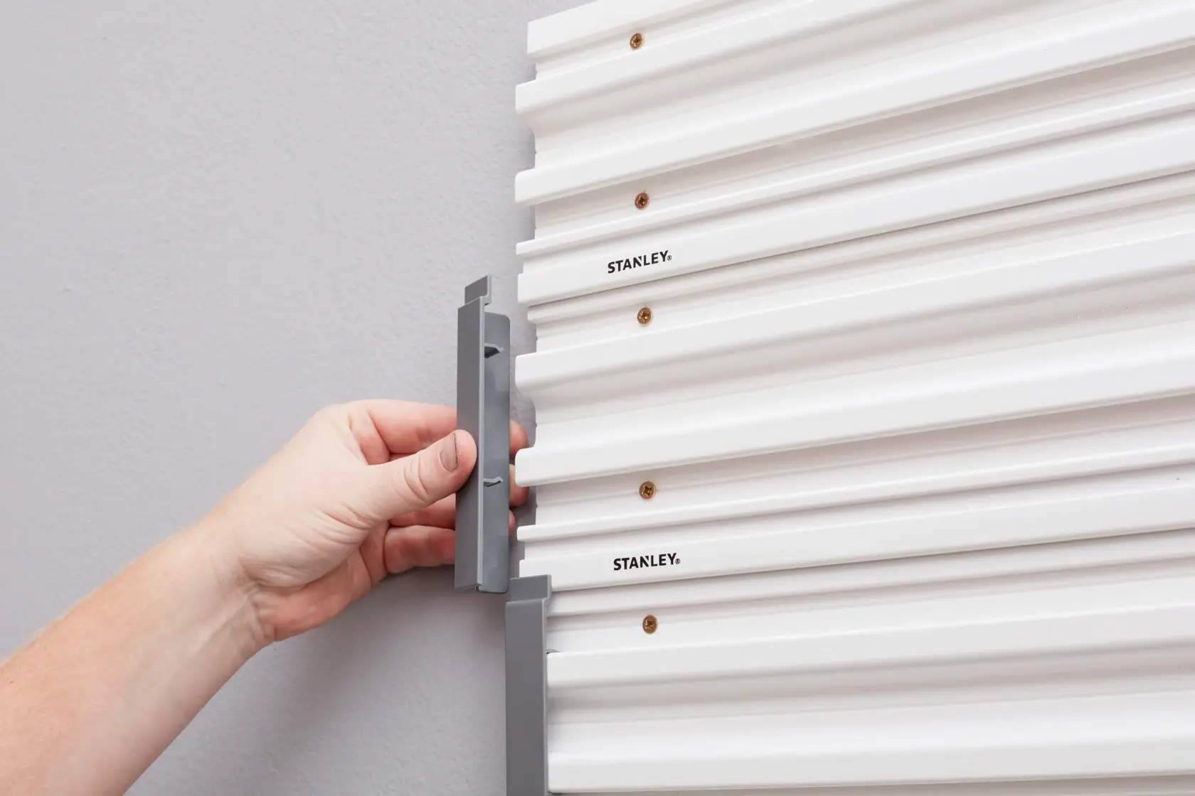 STANLEY STST82611-1 hand installing gray hook on white wall panel, close-up side angle.