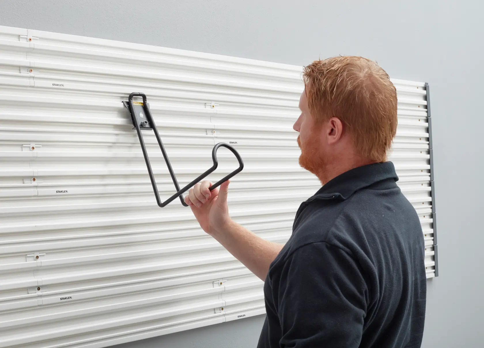 Person mounting STANLEY STST82614-1 wall hook on white wall panel system, side view.