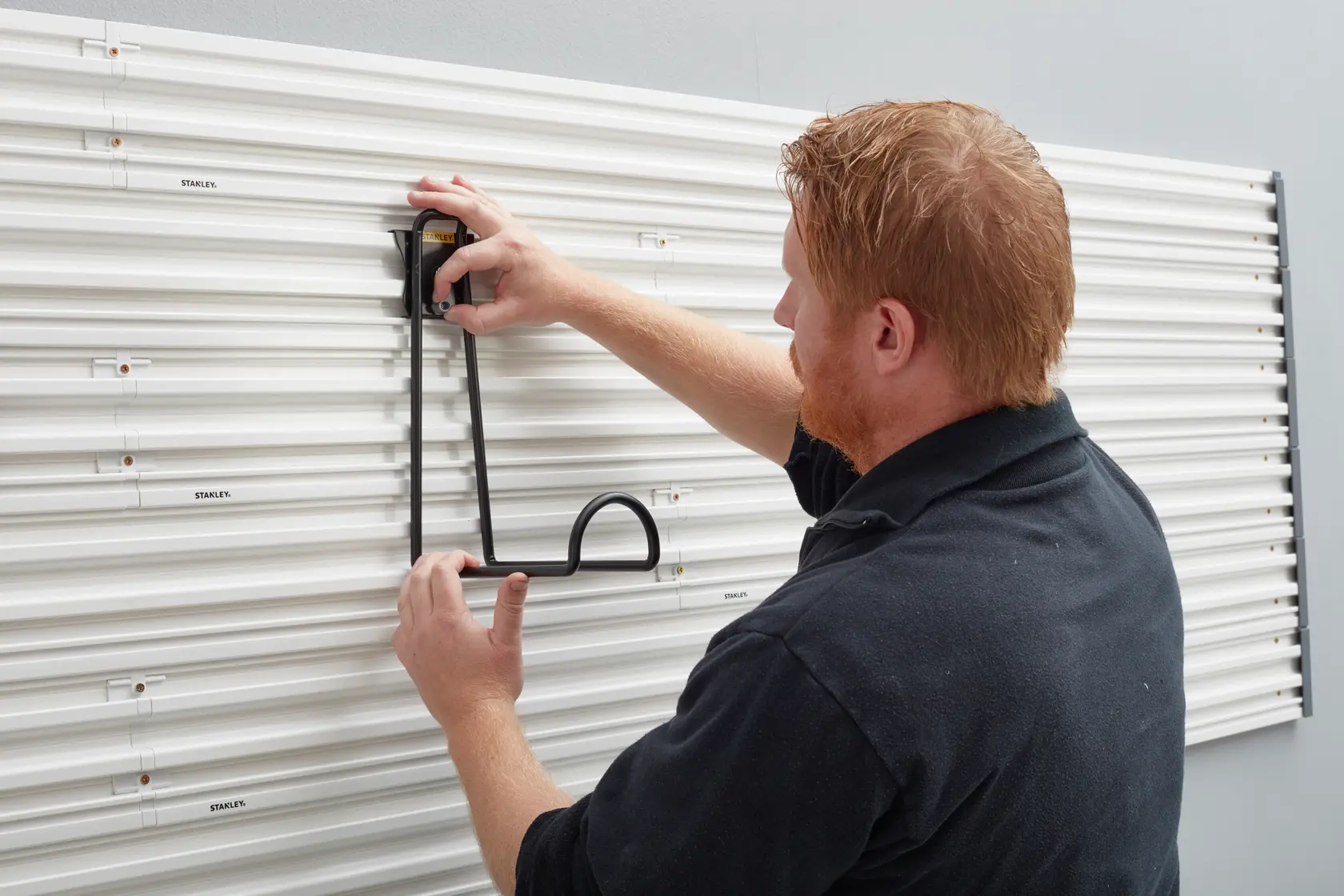 Photo of STANLEY STST82614-1 wall storage hook being mounted on white slatwall panel, side angle.