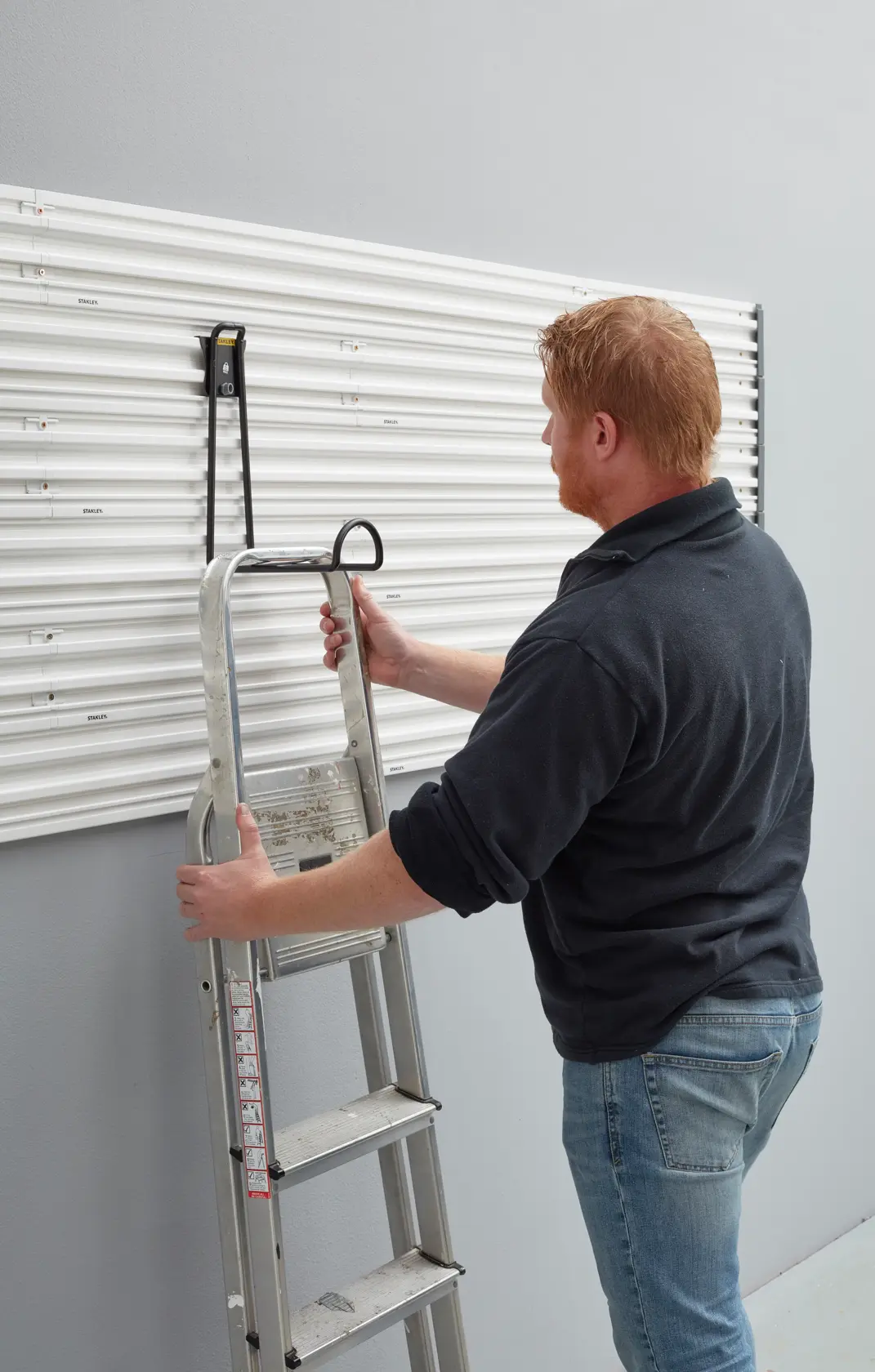 STANLEY STST82614-1 wall hook holding a metal ladder on a white slat wall, side angle photo.