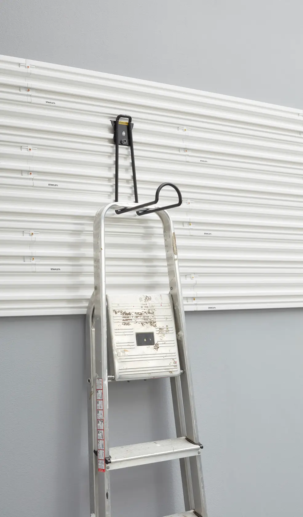 STANLEY STST82614-1 ladder hanging hook on white wall panel, front angle.