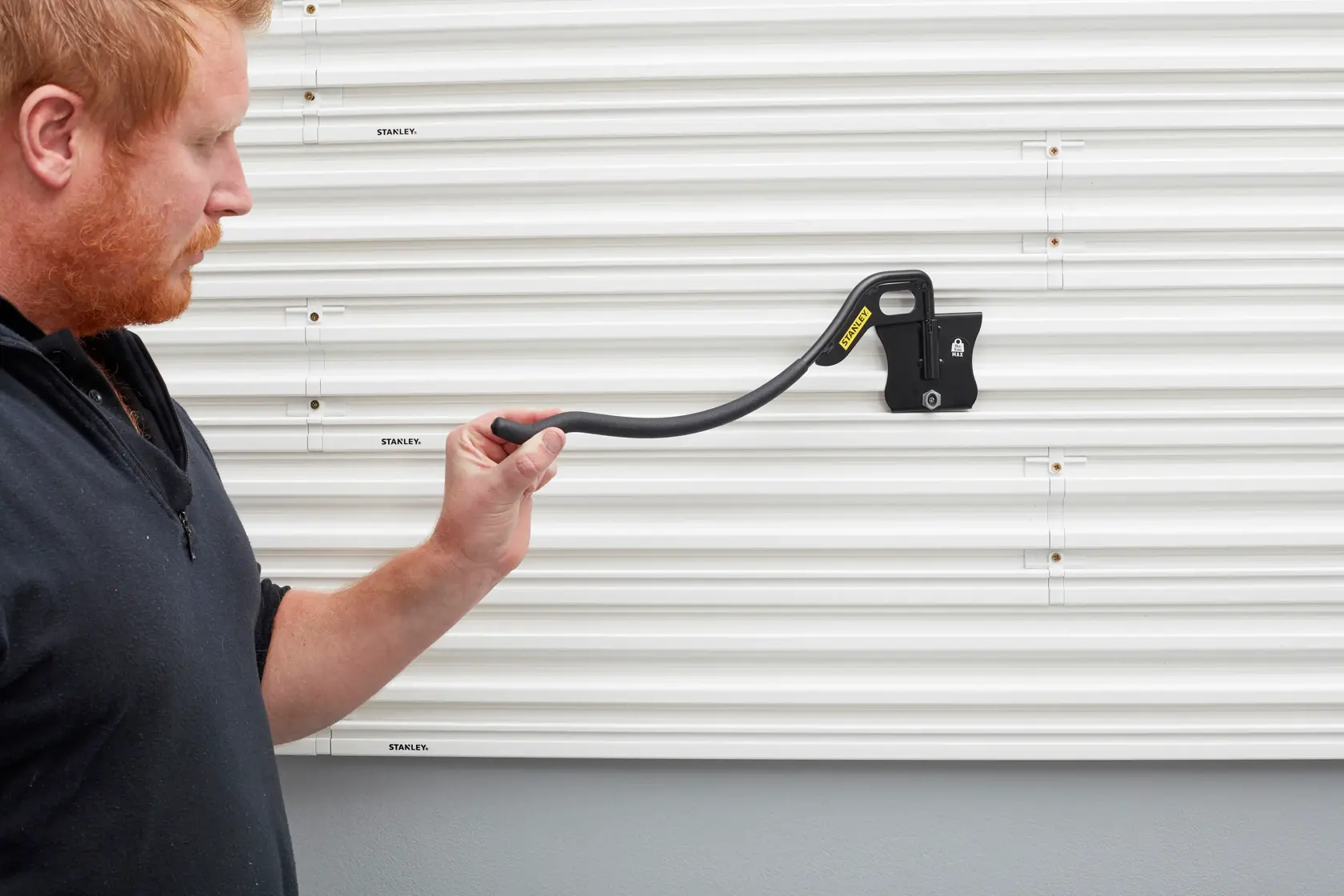 Photo of STANLEY STST82615-1 wall-mounted bracket hook held by a person, on white slatted wall panel.