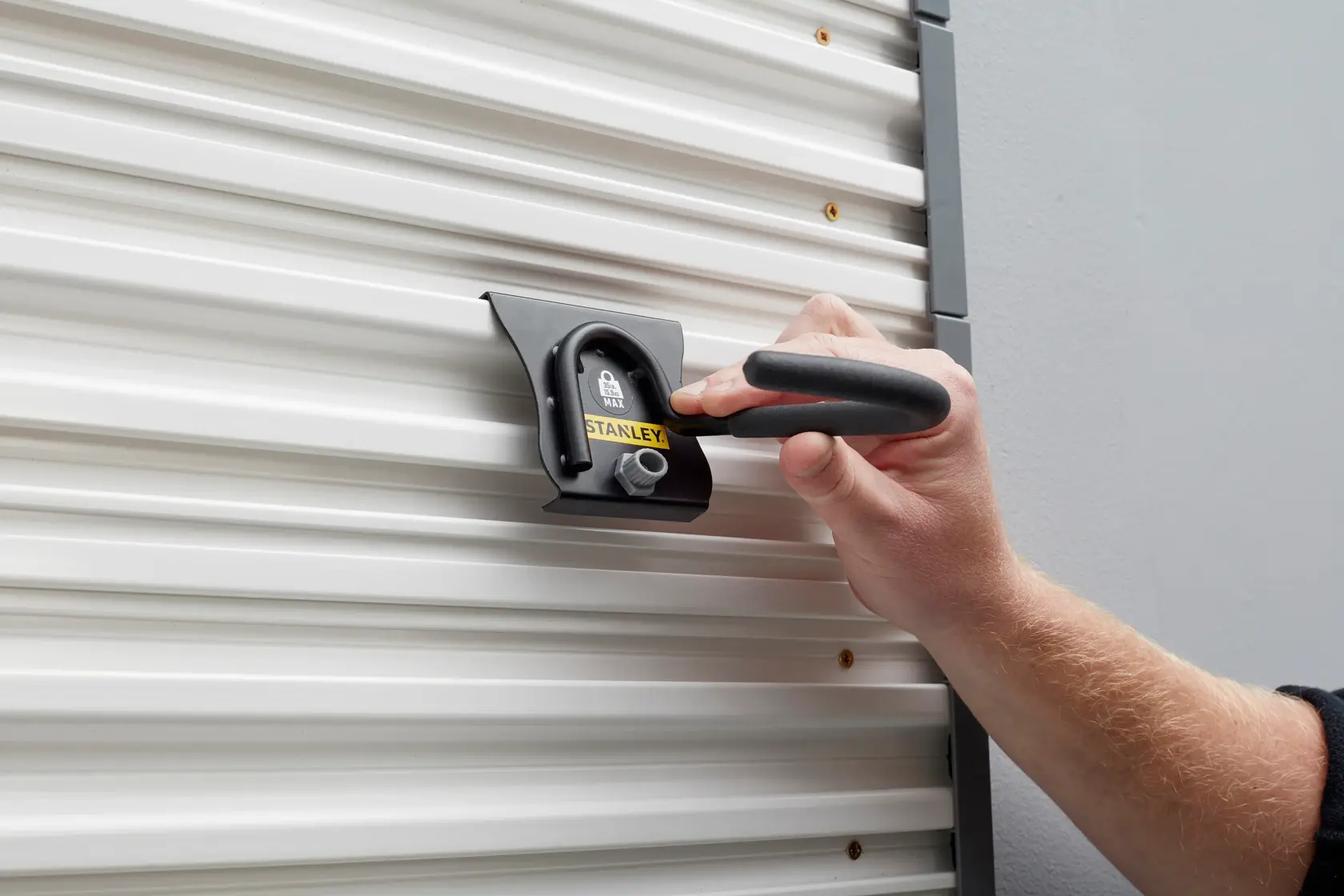 STANLEY STST82616-1 wall-mounted metal hook being used on a corrugated white panel, close-up view.