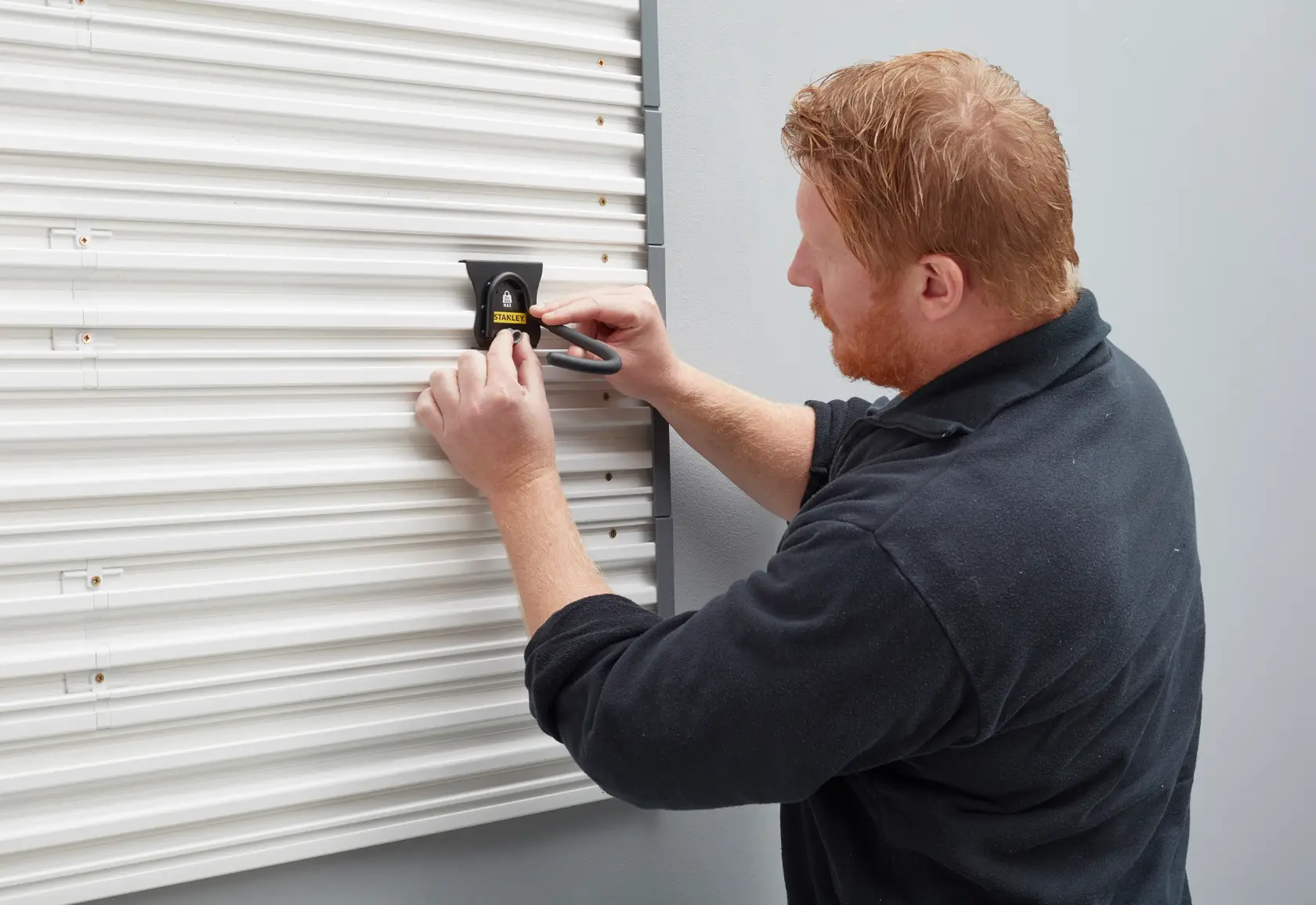 Stanley STST82616-1 wall hook being installed on a white corrugated wall by a person.
