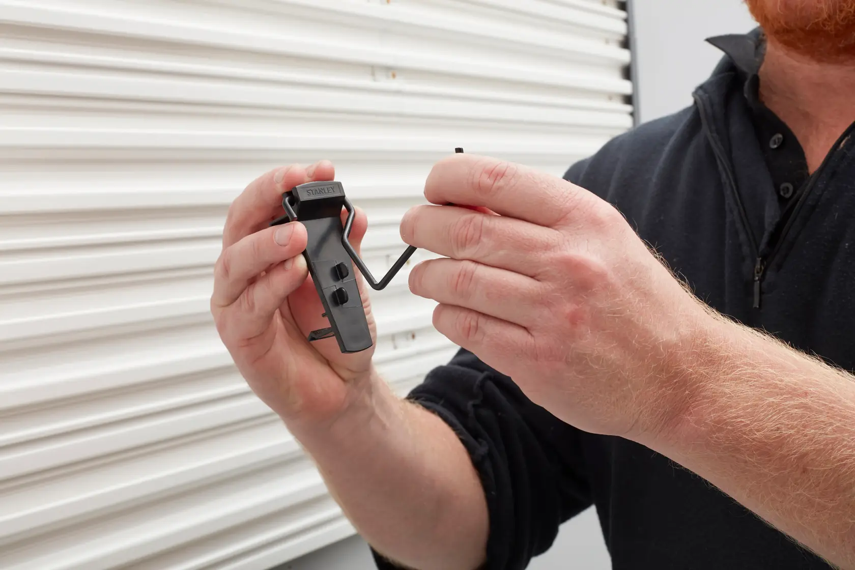 Photo of STANLEY STST82617-1 black tool hook being held by a person in front of a white roller shutter.